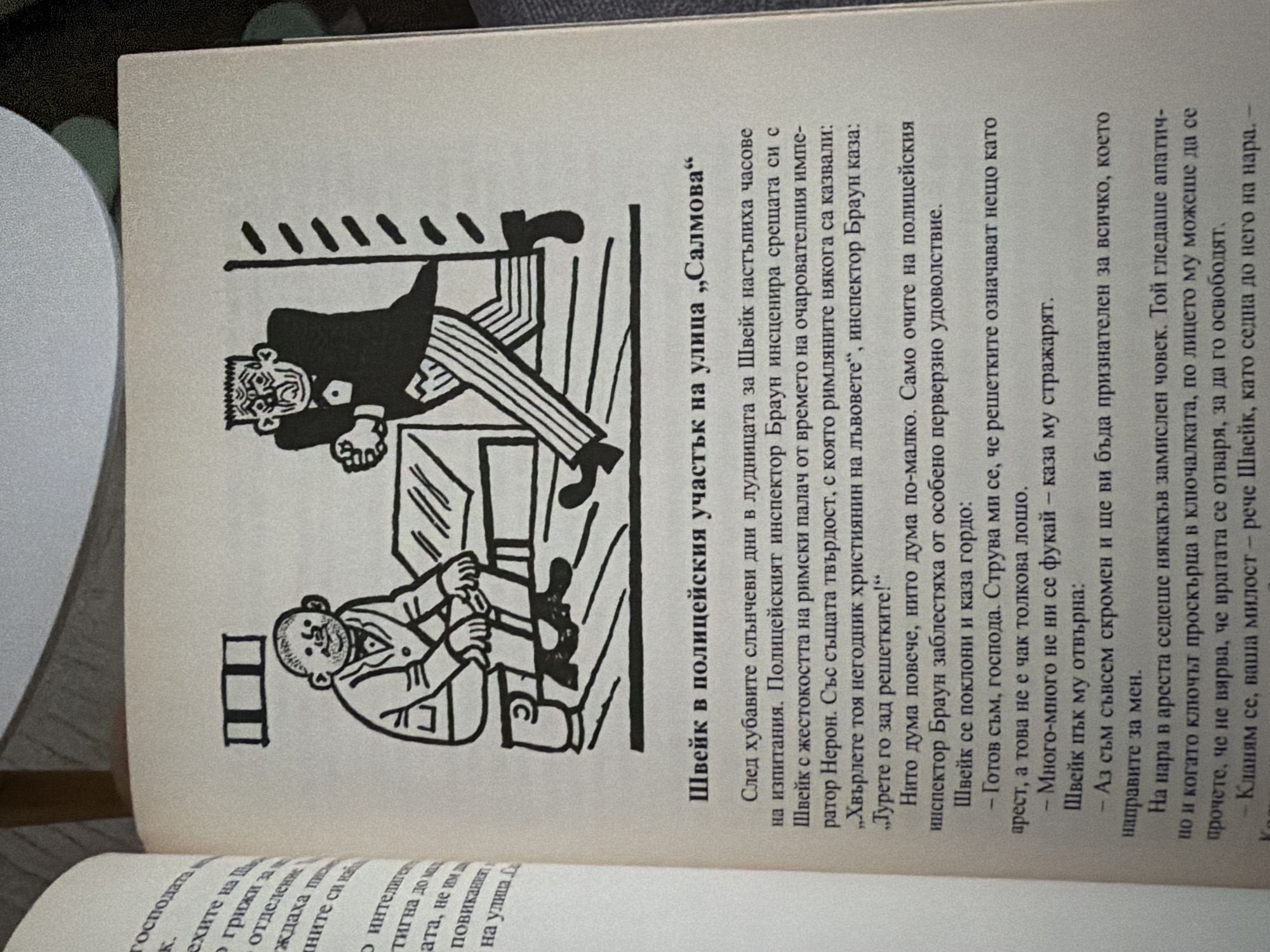 The image shows a page from a book with a black and white illustration and text. The illustration depicts two cartoonish figures in a room. One figure, seated on a chair, appears to be a man with a round face, wearing a suit and bow tie. The other figure, standing, is a stern-looking man with a sharp facial expression, wearing a suit and tie. The text below the illustration is in Cyrillic script and appears to be a narrative, possibly from a story or novel. The title above the text reads "Швейк в полицейския участък на улица „Салмова“" which translates to "Švejk in the police station on Šalmov Street". This title suggests a scene taking place in a police station on Šalmov Street. The rest of the text describes an interaction or event involving Švejk, presumably the seated figure, and the police inspector, presumably the standing figure. The overall scene suggests a humorous or dramatic encounter within a police station setting. The image does not provide any information or visual cues that would allow for identification of the city of Pazardzhik, Bulgaria.