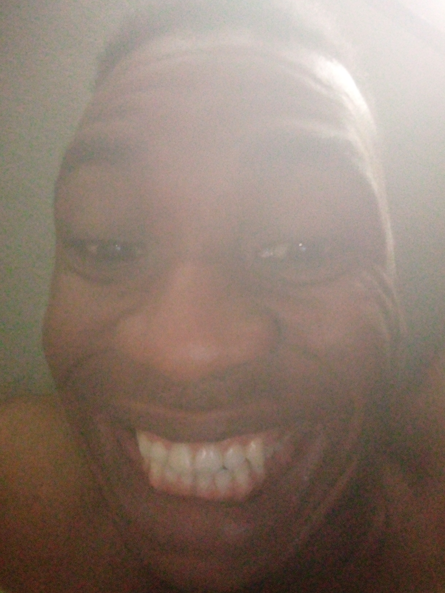 A close-up, foggy photograph shows the face of a dark-skinned person smiling broadly, revealing their teeth. It is difficult to determine the exact location in Ikorodu, Nigeria due to the lack of environmental context.