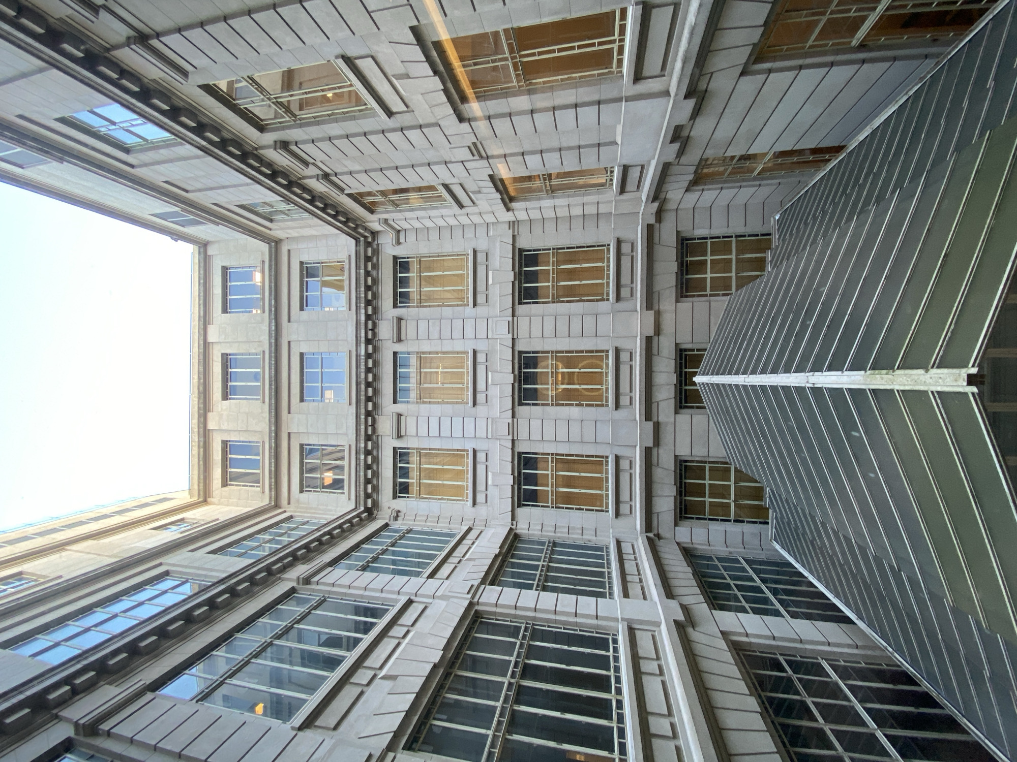 Looking directly up at a building facade. The building is constructed of grey stone with windows. There is a clear sky above, and a sloped structure is on the right side of the frame. The location is Buenos Aires, Argentina.