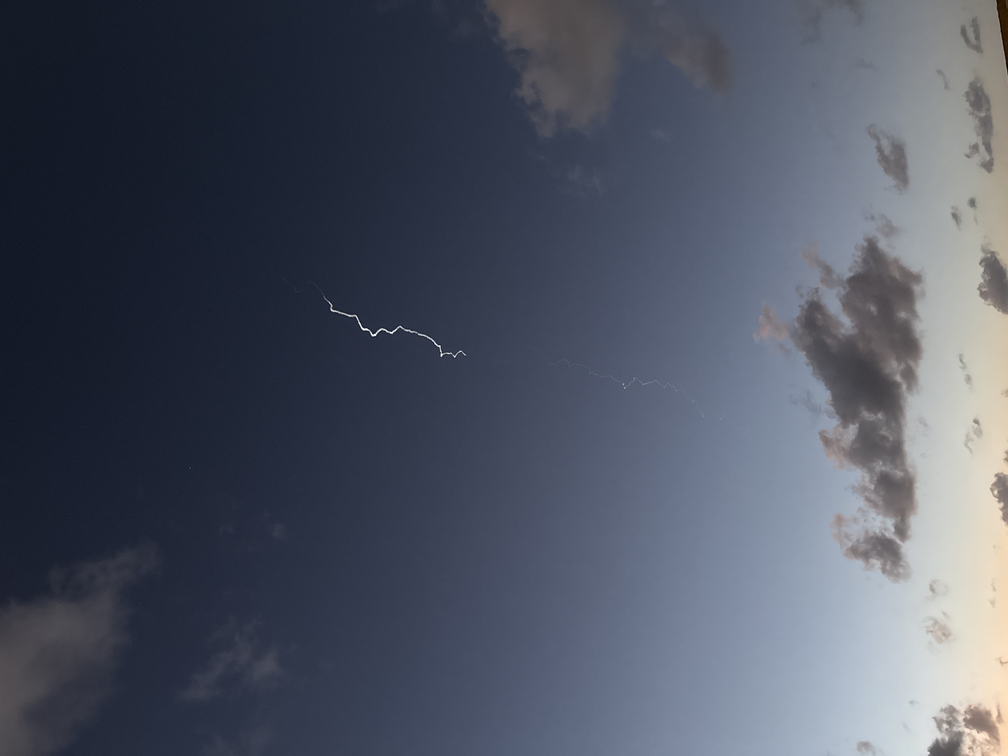 The image depicts a lightning strike in the sky, captured during twilight, as suggested by the color gradient in the clouds. The lightning appears as a bright, jagged line across the left side of the image, and it continues, fainter, towards the right, creating an S-shaped arc. Clouds are visible on both sides of the image, and the sky is dark, but not fully night, suggesting the time of day. Given the image, I can neither confirm nor deny the location is Tel-Aviv, Israel. There are no people or man-made objects clearly visible.