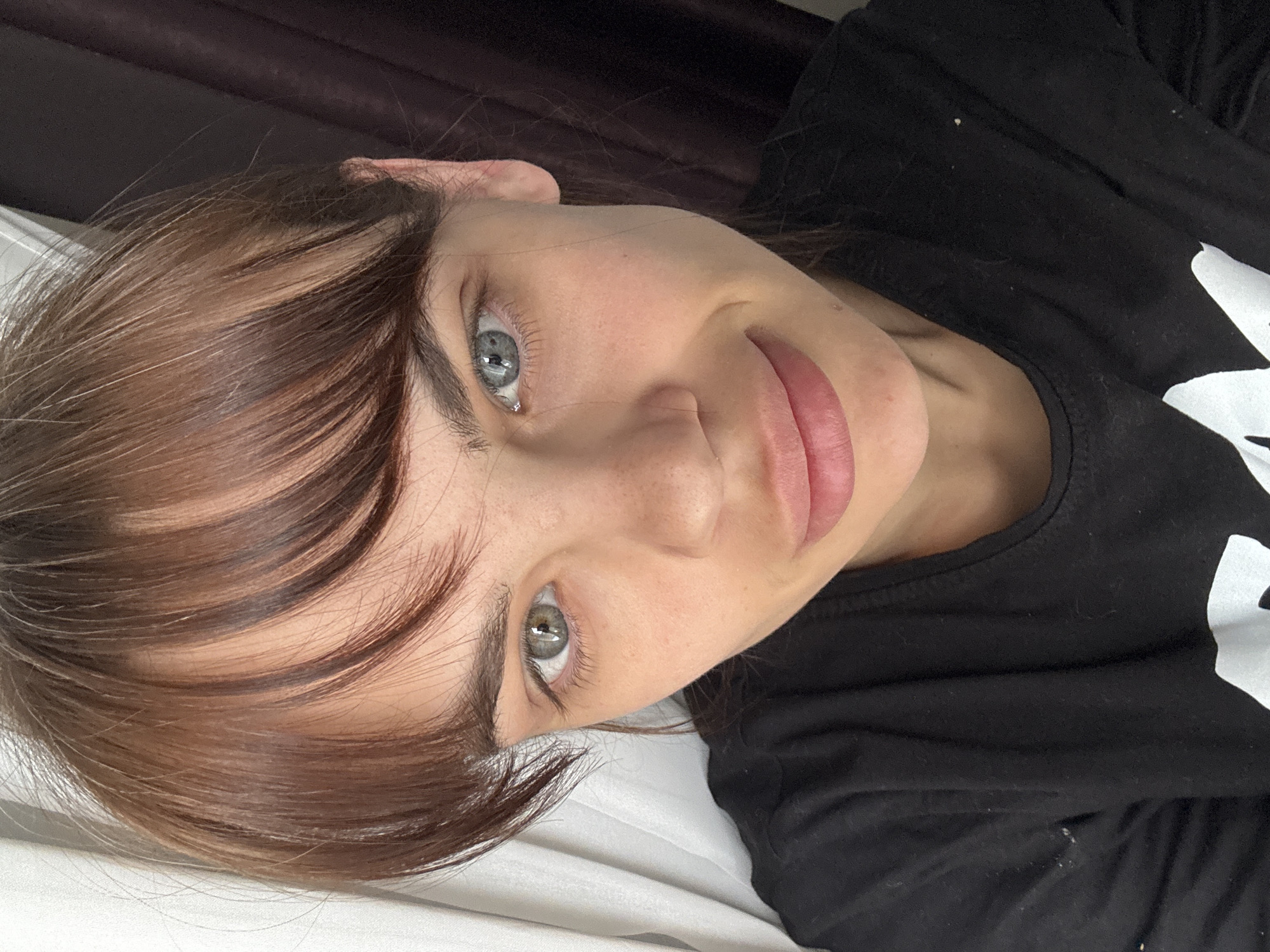 A woman with brown hair and light eyes is lying on a white surface. She is wearing a black shirt. The background appears to be a dark curtain. There is no evidence to suggest the location is Rostov-on-Don, Russia.