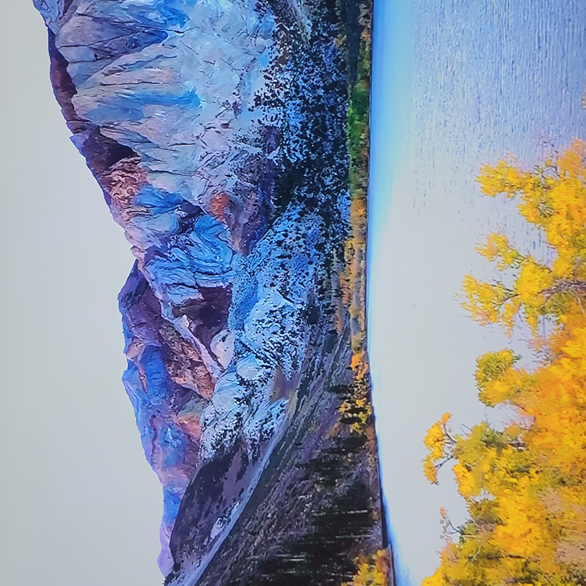 The image presents a landscape featuring a mountain range, a body of water, and foliage. The mountains are rendered in shades of blue, purple, and gray, with textures suggesting rock formations and possibly snow. The water appears calm, reflecting the colors of the sky. Trees with yellow leaves occupy the foreground, indicating autumn. The image is a landscape; there is no indication of it being taken in Yerevan, Armenia. There are no people visible.
