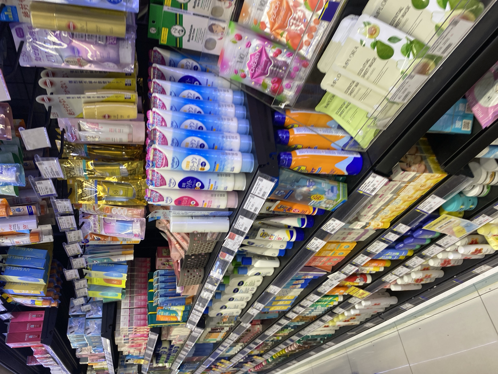 The image shows a retail store aisle, specifically a section dedicated to beauty and personal care products. The shelves are stocked with a variety of items, including sunscreen bottles and tubes, lotions, and face masks. Many of the products are displayed in their original packaging, with some items hanging on hooks and others arranged on the shelves. The overall impression is one of abundance and a wide selection of goods. The lighting appears to be typical of an indoor retail environment. The specific location of Banda Aceh, Indonesia, is not evident from the visual cues in the image itself.