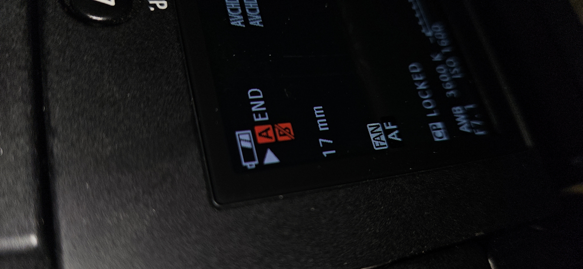 A close-up shot captures the illuminated display screen of a black digital camera or video recorder, held at an angle in Bac Nha Trang Ward, Vietnam. The textured black casing of the device is visible around the screen. The display shows various operational settings and indicators. Visible text includes "AVCHD" (twice), a battery icon (partially filled) next to "A END" and another "A" and "B" icon, "17 mm" (likely focal length), and "FAN AF" (possibly Fan Autofocus). Further settings visible are "GP LOCKED" (indicating a locked general purpose or GPS setting), "AWB 3600 K" (Auto White Balance at 3600 Kelvin), "F7.1" (aperture), and "ISO 1600" (ISO sensitivity). The screen features white and red text against a dark background, suggesting a low-light environment or power-saving display. The background is out of focus, highlighting the device's screen.