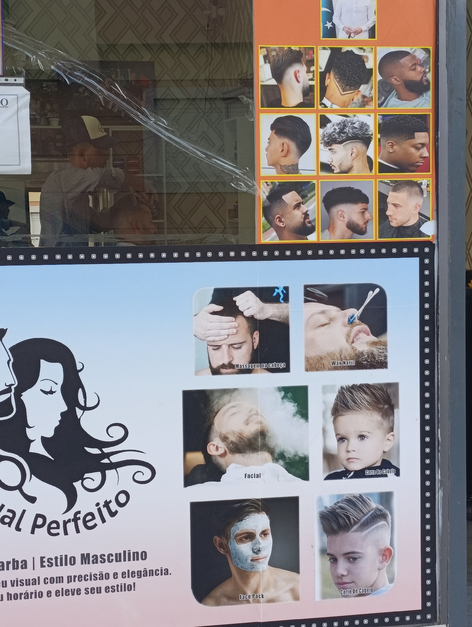 The image displays a storefront window of a barbershop in Setúbal, Portugal. The window is covered with a protective plastic film and contains an advertisement featuring various male hairstyles and grooming services.
The advertisement is divided into sections. The top section showcases nine images of men with different haircuts, ranging from fades and undercuts to styled curls. One image at the very top shows a person in a white shirt.
The bottom section of the advertisement features a large graphic of a stylized male and female silhouette, followed by text in Portuguese. The text appears to be promotional, mentioning "Barba | Estilo Masculino" (Beard | Masculine Style) and encouraging customers to "eu visual com precisão e elegância. eu horário e eleve seu estilo!" (visual with precision and elegance. my schedule and elevate your style!).
Below the graphic and text, there are six smaller images illustrating grooming services. These include:
* A close-up of a man's head with hands massaging his scalp, labeled "Massagem na cabeça" (Scalp Massage).
* A man undergoing a nasal wax treatment, labeled "Wax Nariz" (Nose Wax).
* A man with steam around his face, labeled "Facial".
* A young boy with styled hair, labeled "Corte De Cabelo" (Haircut).
* A man with a face mask, labeled "Face Pack".
* A young boy with an elaborate haircut, labeled "Corte De Cabelo" (Haircut).
In the background, through the plastic film and the shop window, a person wearing a baseball cap is visible, possibly an employee or customer, interacting with someone or something inside the barbershop. The interior of the shop has shelves with products, and patterned wallpaper is visible on the back wall. The overall scene suggests a vibrant, modern barbershop aiming to attract customers with a variety of styling and grooming options.