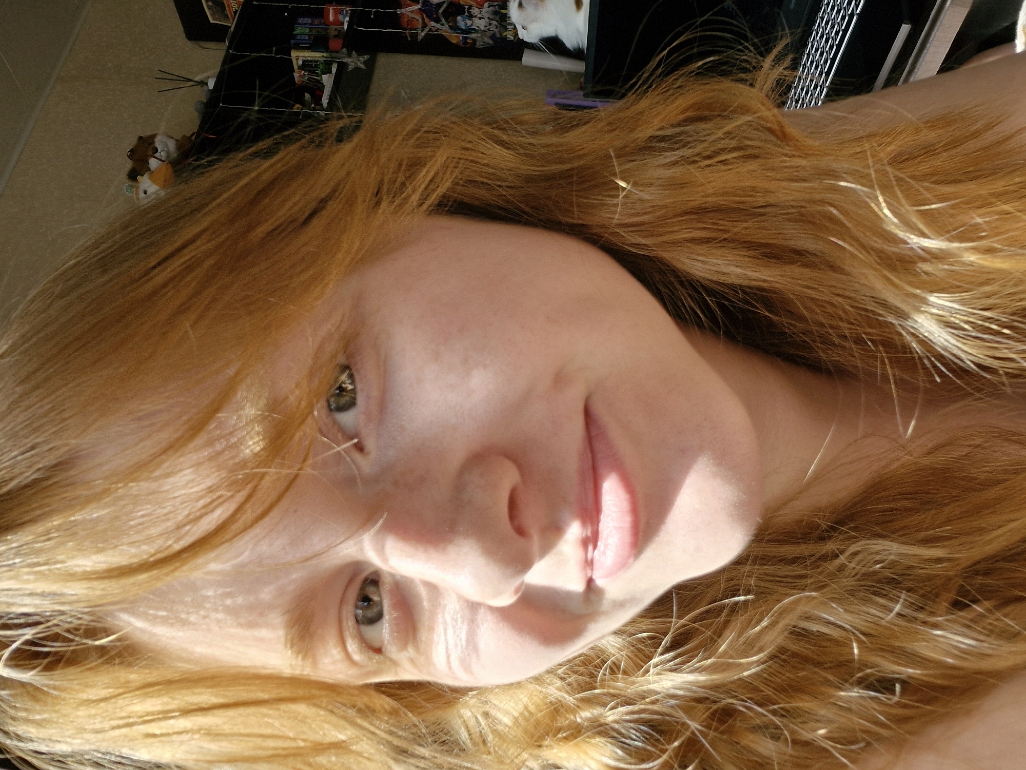 A fair-skinned person with red hair is lying down indoors. The person's face is angled toward the camera. The lighting appears to be natural, casting shadows across the face. In the background, there is a shelf containing items and possibly a pet. The location of this image is not specified or visually identifiable from the image, and there is no mention of the city of Yekaterinburg, Russia.