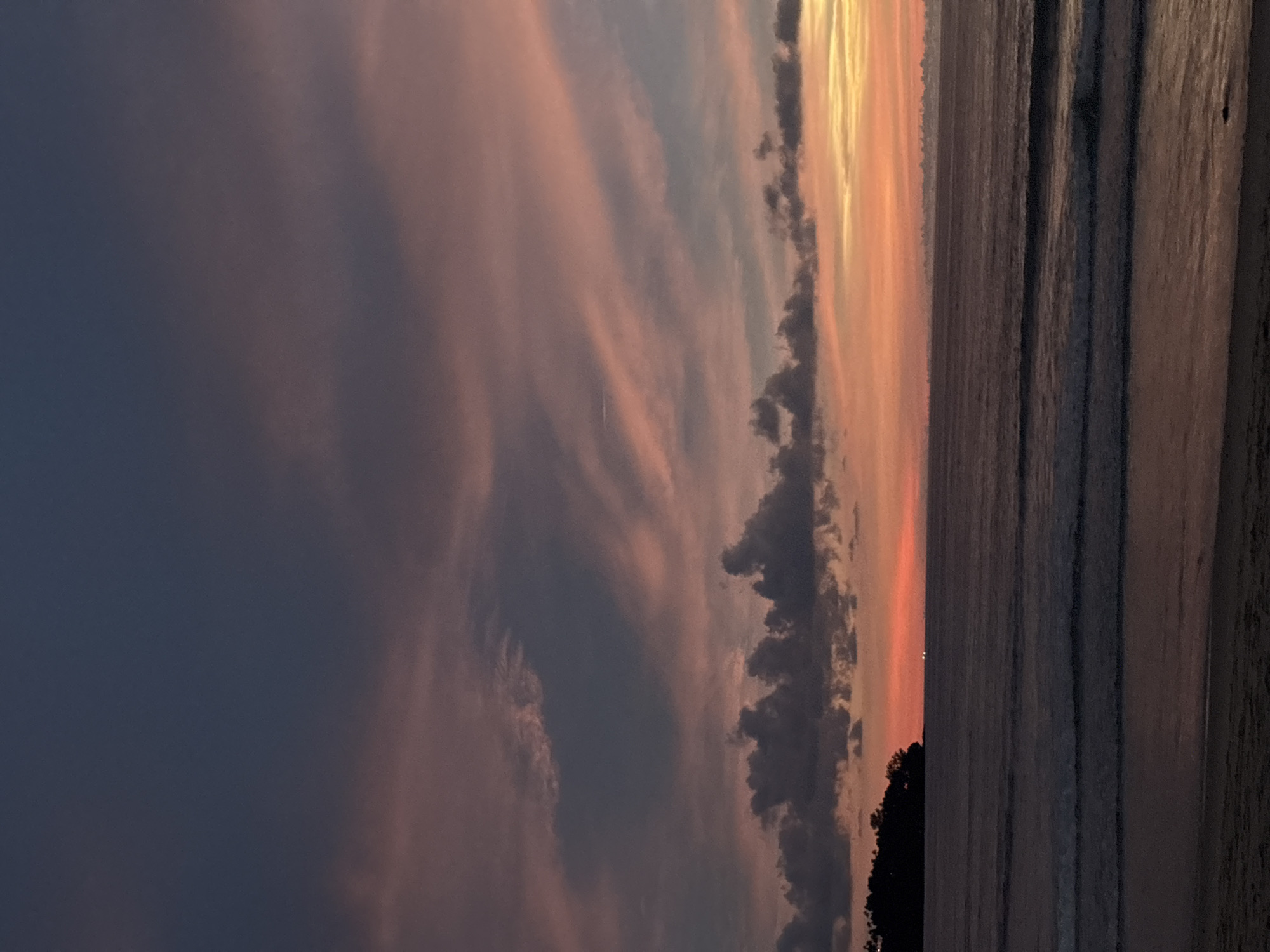 A serene sunset paints the sky in hues of pink, purple, and orange over the Andaman Sea at Choeng Thale, Thailand. The silhouette of a verdant headland juts out into the calm water on the left, adding a touch of natural beauty to the coastal landscape. Gentle waves lap against the sandy shore, reflecting the soft glow of the fading light. The scene evokes a sense of peace and tranquility, a perfect moment captured at the end of a day in this tropical paradise.