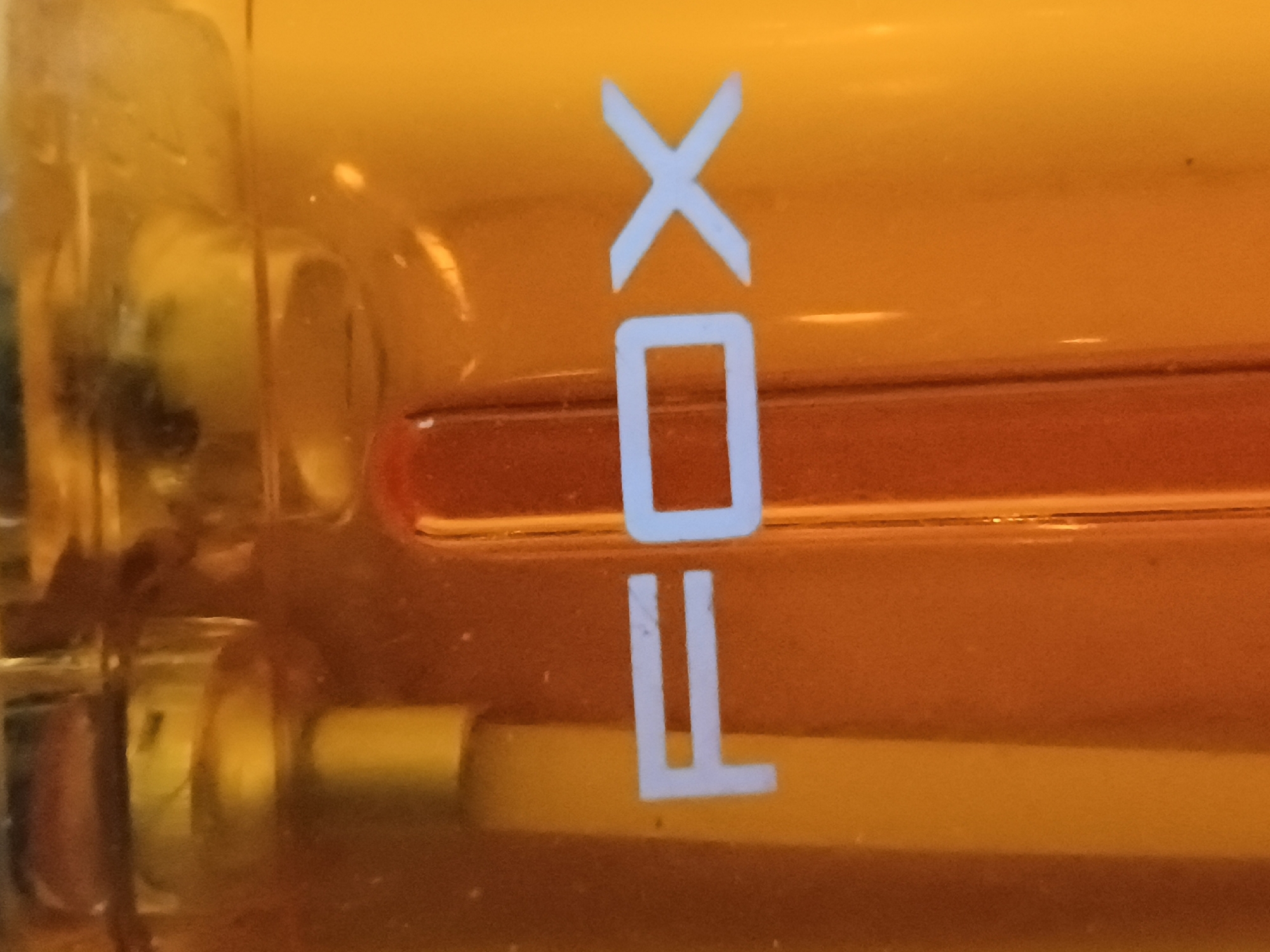 This media file shows a close-up view of an orange-colored glass object, likely a light bulb, with white text printed on it. The text appears to spell "FOX" vertically, with each letter clearly visible. The "F" is at the bottom, followed by "O" and then "X" at the top. The letters are simple, sans-serif, and appear to be embossed or printed onto the surface of the glass.
The background is a gradient of orange, transitioning from a lighter shade at the top to a darker, reddish-orange at the bottom. There are some reflective surfaces and subtle textures visible on the glass, suggesting it's a manufactured item. A faint yellow cylindrical element is visible below the "F", possibly part of the internal structure of the light bulb. There are also some out-of-focus dark shapes on the left side, which might be part of the surrounding environment or the object holding the light bulb.
The lighting is warm and appears to be coming from within or behind the object, illuminating the text and the orange glass. No specific time of day or weather conditions can be inferred from the image. The setting is ambiguous, but the nature of the object suggests an indoor or controlled environment. There are no people or discernible emotional cues.
The prominent text visible is "FOX". The location context of Zaporizhzhia, Ukraine, is provided but not visually evident within the image itself.