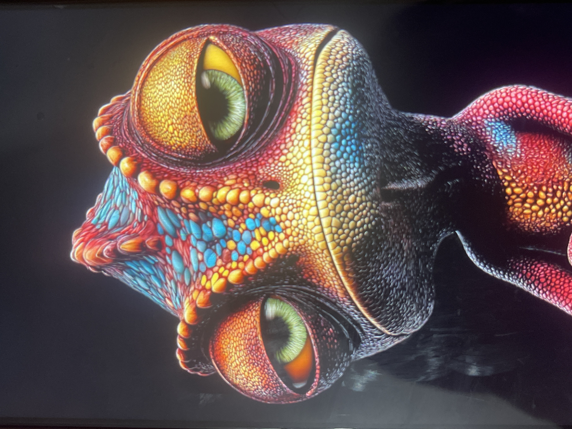 The image is a close-up, head-on portrait of a CGI chameleon against a black background. The chameleon has large, expressive eyes with green irises and yellow sclera. Its skin is textured and brightly colored, with scales ranging from red and orange to yellow and blue. The chameleon has a prominent crest on its head and a slightly downturned mouth, giving it a somewhat weary or grumpy expression. The lighting is dramatic, highlighting the details of the chameleon's skin and features. There is no discernible location in Bishkek City, Kyrgyzstan; the image appears to be a piece of digital art or animation.