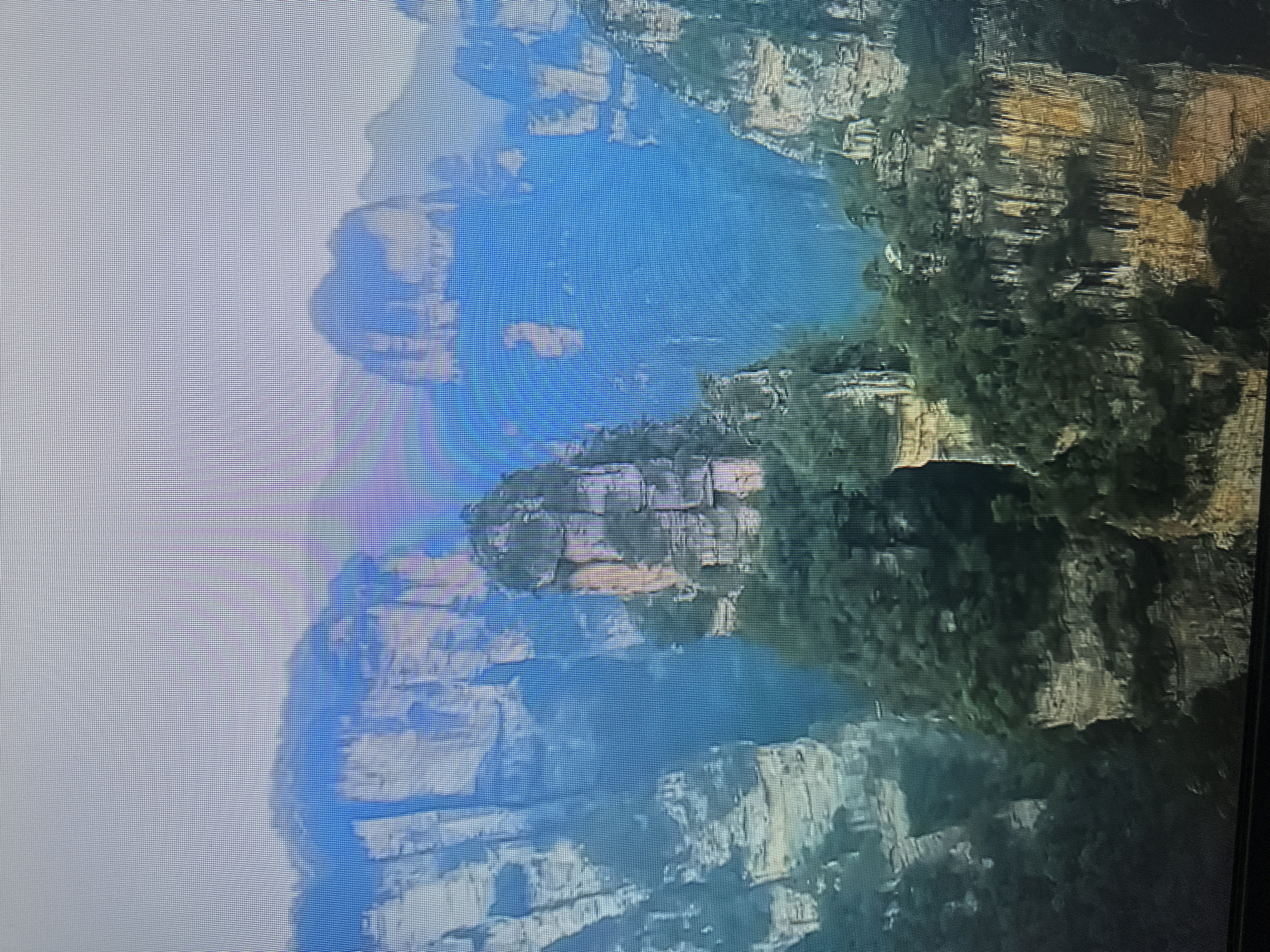 The image shows a panoramic view of a mountainous landscape with towering, slender rock formations covered in lush green vegetation. The formations are characterized by sheer cliffs and flat tops, with some appearing to be sandstone or similar sedimentary rock. Mist or fog partially obscures some of the distant peaks, creating a sense of depth and scale. The sky is overcast with a pale, diffused light. The overall scene depicts a natural wonder, likely a national park or protected area known for its unique geological features. There is no indication that this image is related to the city of Kyiv, Ukraine.