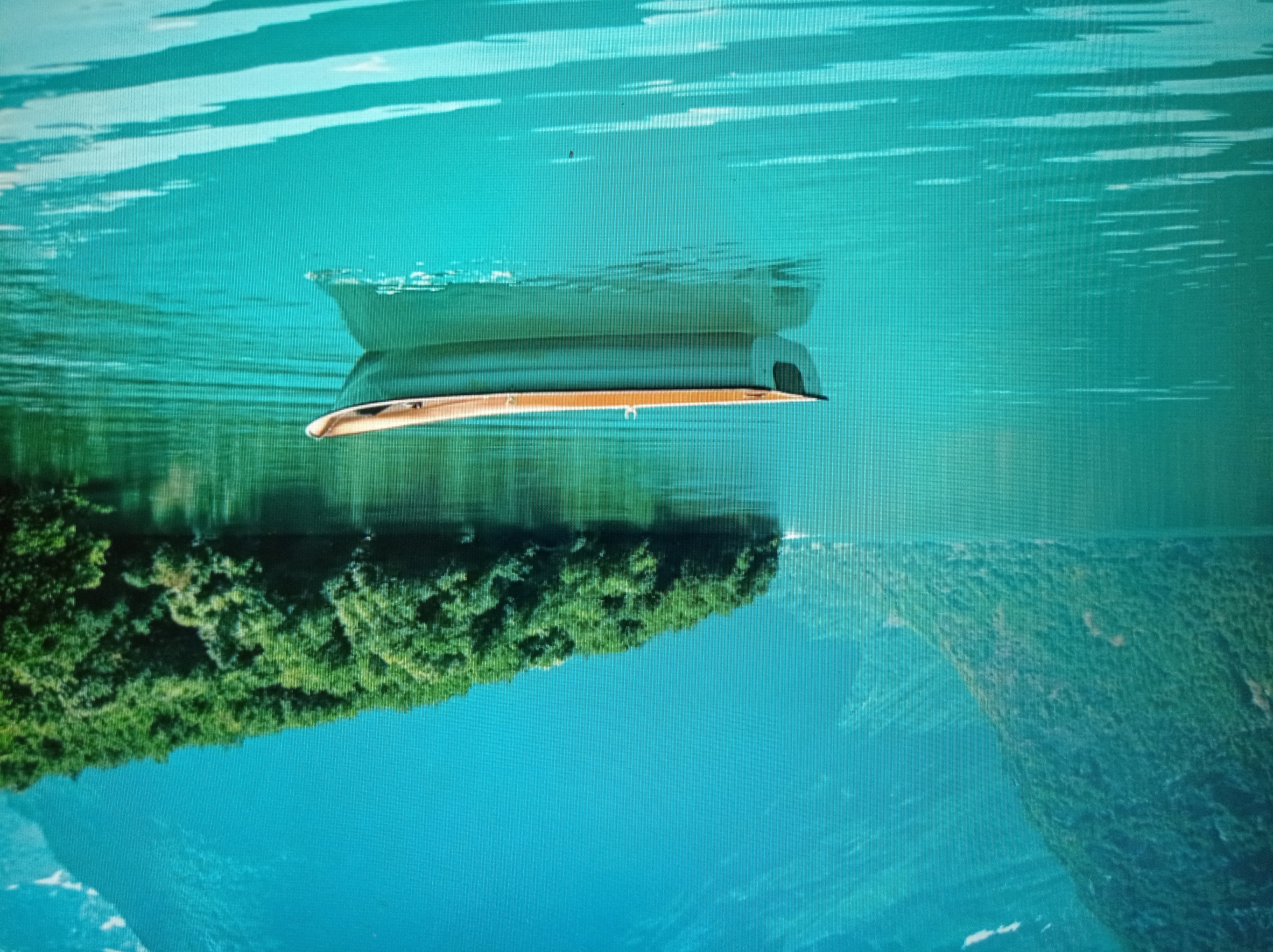 A single, narrow, wooden boat with a light-colored interior and dark exterior floats on calm, turquoise water. The boat is positioned in the lower center of the frame, slightly to the left. In the background, to the left, a steep, tree-covered mountainside slopes down towards the water. To the right, a dense green forest covers a sloping hillside that extends into the water. The water's surface is still, reflecting the sky and the surrounding landscape. The overall scene depicts a serene natural landscape with a boat as the sole human-made element. This image is not located in the city of Mukachevo, Ukraine; it depicts a natural water body surrounded by mountains and forests, possibly a fjord or lake in a mountainous region.