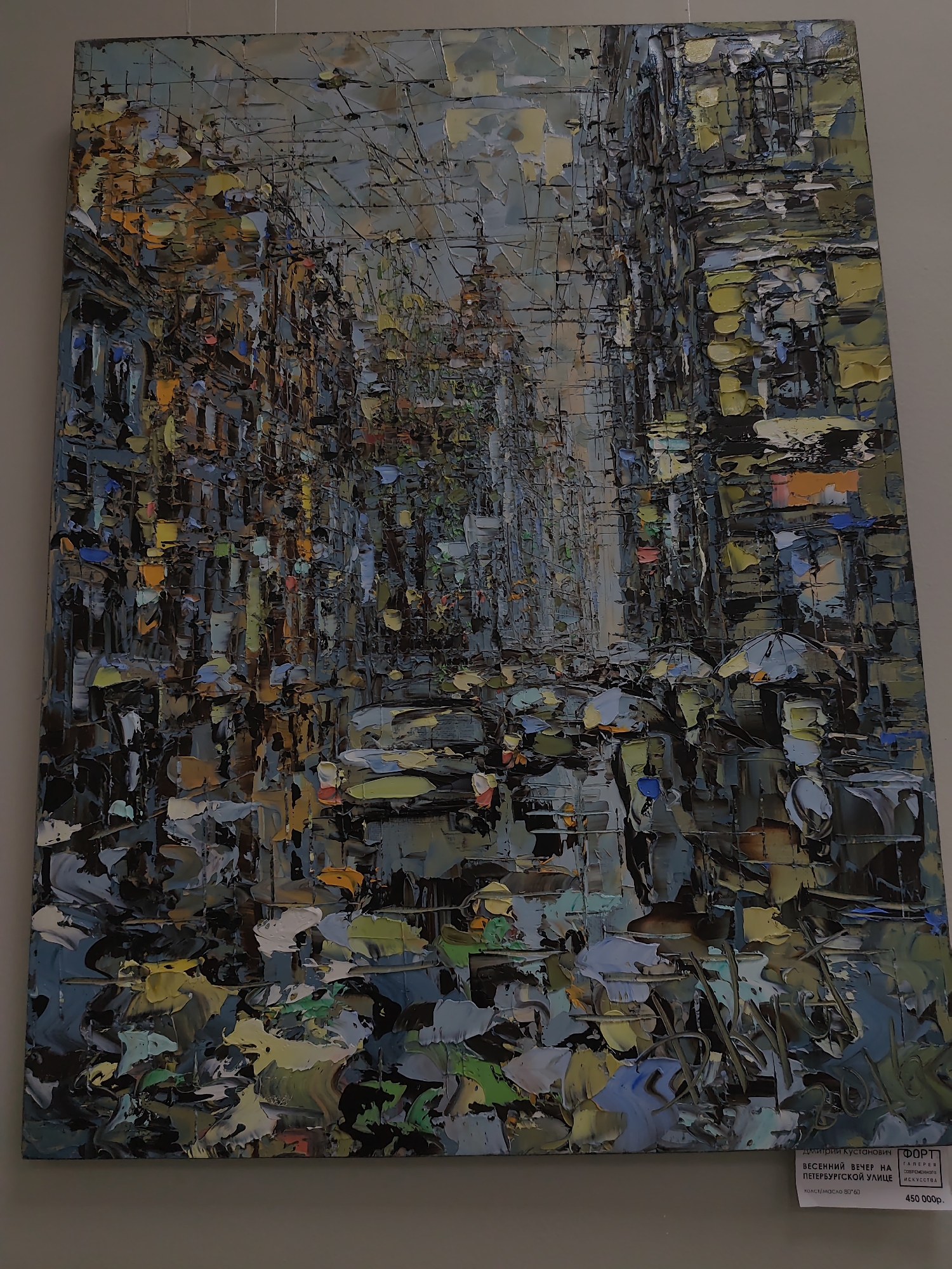 This is a textured, impressionistic oil painting on canvas depicting a city street scene. The painting is characterized by thick, impasto brushstrokes that create a sense of depth and movement.
The subjects are a crowd of people walking under umbrellas, suggesting a rainy or overcast day. The figures are abstractly rendered, with their forms suggested by patches of color and texture. Several cars are also visible on the street, adding to the urban setting. The buildings on either side of the street are depicted with a similar textural approach, their windows and architectural details rendered as a mosaic of colors.
The overall impression is one of a bustling city on a cool, possibly damp, spring evening. The colors are muted but vibrant, with blues, grays, yellows, and oranges dominating the palette. The light appears diffused, consistent with overcast weather. The painting evokes a sense of atmosphere and the transient beauty of urban life.
A label at the bottom right of the painting provides textual information. It reads: "ДМИТРИЙ КУСТАНОВИЧ ФОРТ ВЕСЕННИЙ ВЕЧЕР НА ПЕТЕРБУРГСКОЙ УЛИЦЕ холст/масло 80*60 ГАЛЕРЕЯ СОВРЕМЕННОГО ИСКУССТВА 450 000р." This translates to: "Dmitry Kustanovich FORT SPRING EVENING ON PETROGRAD STREET canvas/oil 80*60 GALLERY OF CONTEMPORARY ART 450,000 RUB." This identifies the artist, title of the work, medium, dimensions, and price, and indicates it is from a gallery of contemporary art. The location context is Sochi, Russia.