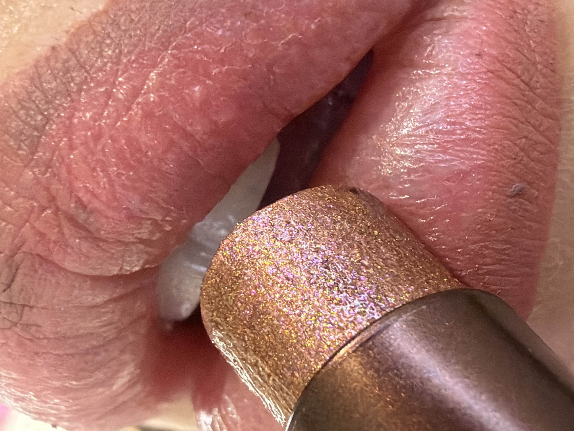 This is a close-up, low-angle, indoor shot of a person's lips. A gold, glittery makeup applicator is positioned in front of the lower lip, with its tip touching the lips. The lips appear dry and have visible texture. The lighting is bright and diffused. The image does not contain enough information to determine the location within Saint Petersburg, Russia.