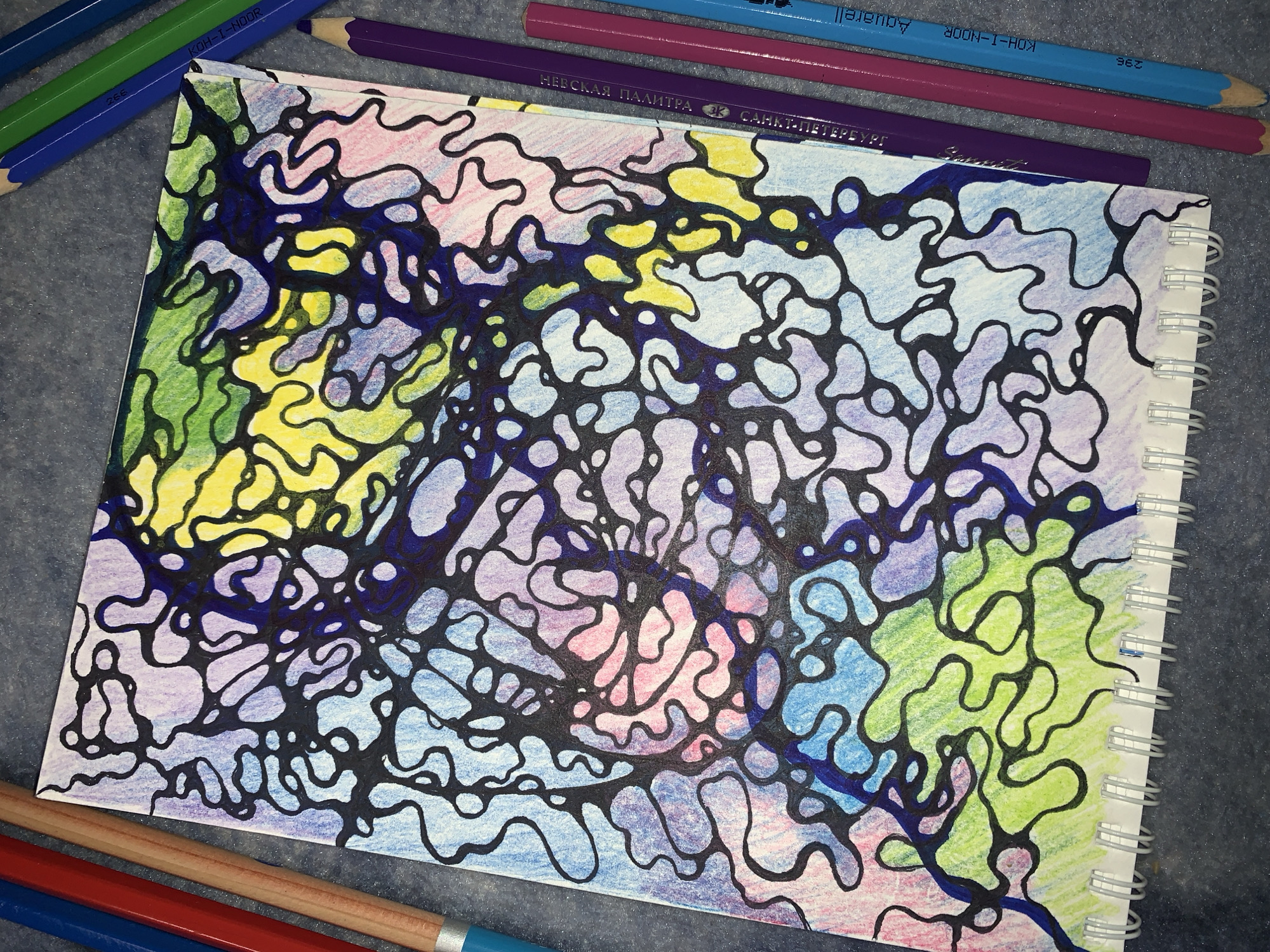 This media file features a top-down, close-up view of a sketchbook page filled with abstract, neurographic art. The artwork is characterized by intricate, black, organic lines that divide the page into various enclosed shapes. These shapes are then filled with a vibrant palette of colored pencils, including shades of green, yellow, pink, purple, and blue, creating a dynamic and energetic composition. The art style suggests a meditative or creative process, with the colors blending and overlapping within the defined boundaries.
Surrounding the sketchbook, several colored pencils are visible, hinting at the tools used to create the artwork. These include blue, green, purple, pink, and light blue pencils, some of which have visible branding. One pencil displays the text "KOH-I-NOOR" and "Aquarell," and another reads "НЕВСКАЯ ПАЛИТРА" in Cyrillic script, with "САНКТ-ПЕТЕРБ" and "БУРГ" also present. The background appears to be a textured, dark surface, possibly a table or fabric, providing a neutral contrast to the colorful artwork. The lighting suggests an indoor setting, with the light source likely positioned above and to the left. The overall impression is one of a creative endeavor, a moment captured during the process of making art.
---
The final answer is:
This media file features a top-down, close-up view of a sketchbook page filled with abstract, neurographic art. The artwork is characterized by intricate, black, organic lines that divide the page into various enclosed shapes. These shapes are then filled with a vibrant palette of colored pencils, including shades of green, yellow, pink, purple, and blue, creating a dynamic and energetic composition. The art style suggests a meditative or creative process, with the colors blending and overlapping within the defined boundaries.
Surrounding the sketchbook, several colored pencils are visible, hinting at the tools used to create the artwork. These include blue, green, purple, pink, and light blue pencils, some of which have visible branding. One pencil displays the text "KOH-I-NOOR" and "Aquarell," and another reads "НЕВСКАЯ ПАЛИТРА" in Cyrillic script, with "САНКТ-ПЕТЕРБ" and "БУРГ" also present. The background appears to be a textured, dark surface, possibly a table or fabric, providing a neutral contrast to the colorful artwork. The lighting suggests an indoor setting, with the light source likely positioned above and to the left. The overall impression is one of a creative endeavor, a moment captured during the process of making art.