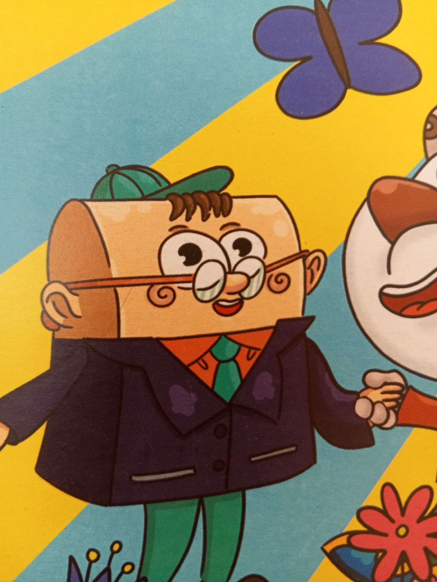 The image shows a close-up of a cartoon illustration featuring two characters. The character on the left is a light brown, cylindrical figure wearing glasses, a dark blue suit over an orange shirt and a green tie, green pants, and a green baseball cap. The character on the right is partially visible and appears to be white with brown accents, with a large open mouth. A purple butterfly with a brown outline is in the upper right corner. The background consists of diagonal stripes of yellow and light blue. There are also stylized flowers at the bottom. The image does not depict any recognizable landmarks or elements that would indicate its location in Chistopol, Russia.