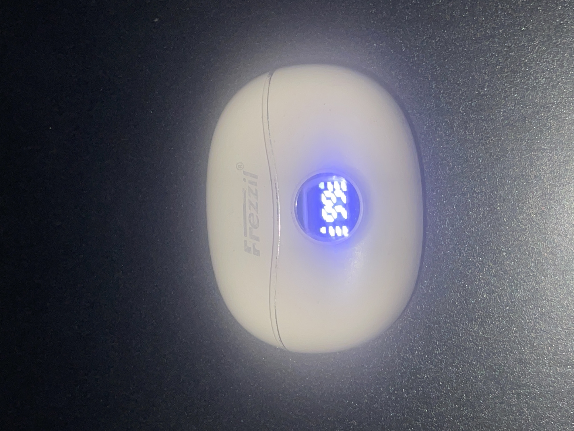 A white, oval-shaped device with the brand name "Frezzzil" on its left side sits on a dark, matte surface. The device has a circular blue-lit display showing "96.6". It's unclear if this is indoors or outdoors but it is impossible to determine if it is located in the city of Abraka, Nigeria, due to the lack of landmarks or other contextual clues.