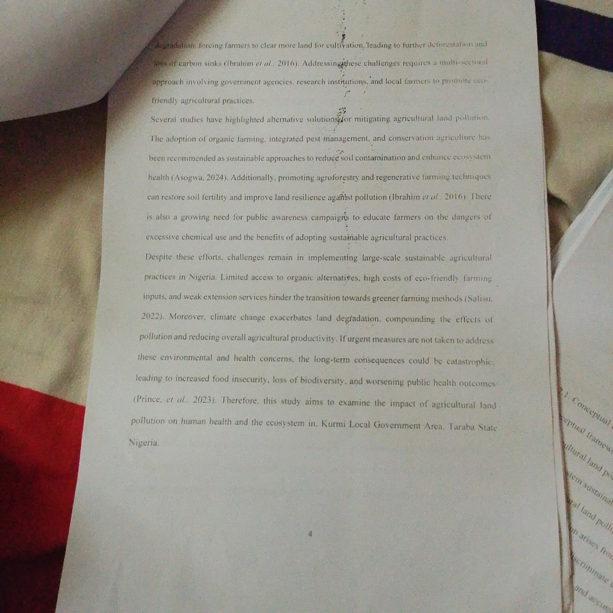 The image shows a close-up of a printed document, likely a research paper or book. The text discusses agricultural land degradation, pollution, and its impact on human health and the ecosystem. Specific topics mentioned include forcing farmers to clear more land, loss of carbon sinks, integrated pest management, agroforestry, and regenerative farming techniques. The document also refers to studies and challenges in implementing sustainable agricultural practices in Nigeria, specifically mentioning the Kurmi Local Government Area in Taraba State. There are no people, discernible environmental features of Jalingo, Nigeria, or specific objects outside of the printed document itself visible in the image. The document appears to be printed on white paper with black text and is partially illuminated by light, casting shadows on its surface.