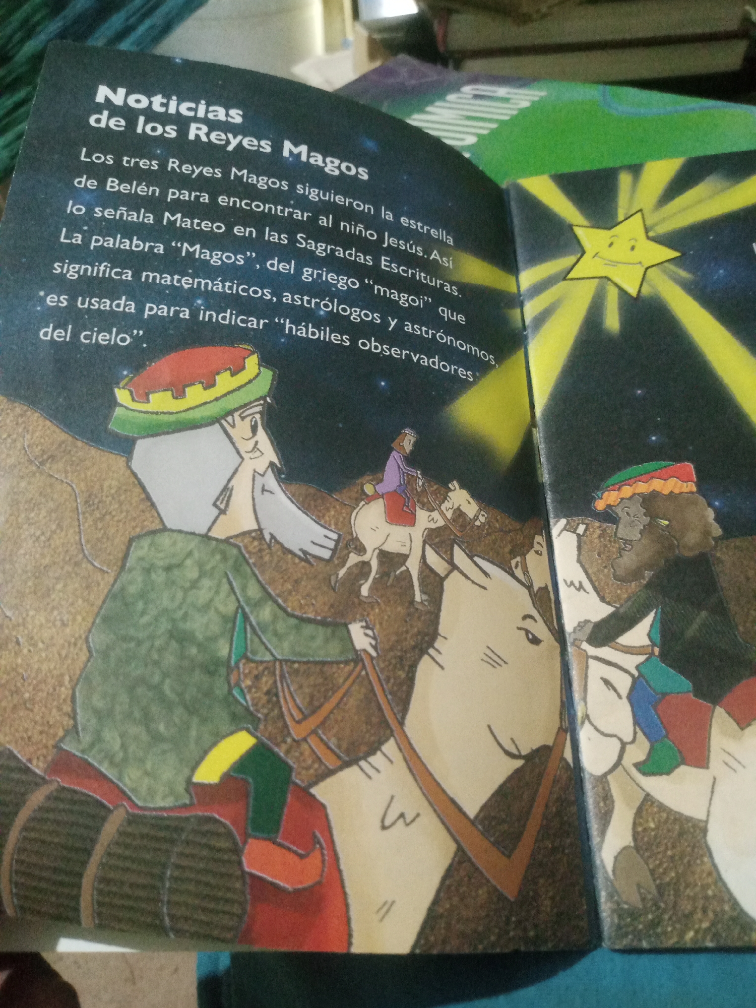 The image shows an open book with illustrations and text in Spanish. The left page features text that reads "Noticias de los Reyes Magos" (News of the Three Wise Men) and continues with a narrative about them. The illustration on this page depicts three figures, presumably the Wise Men, riding on camels, with one figure in the foreground wearing a green cloak and a distinctive hat. The right page shows a yellow star with a face, radiating light, and another illustration of a Wise Man on a camel. The book appears to be a children's book. The background is out of focus and suggests the book is resting on a surface, possibly a table, with other objects visible in the upper portion of the image. There is no discernible information in the image that indicates its location in Santa Ana, Venezuela.
