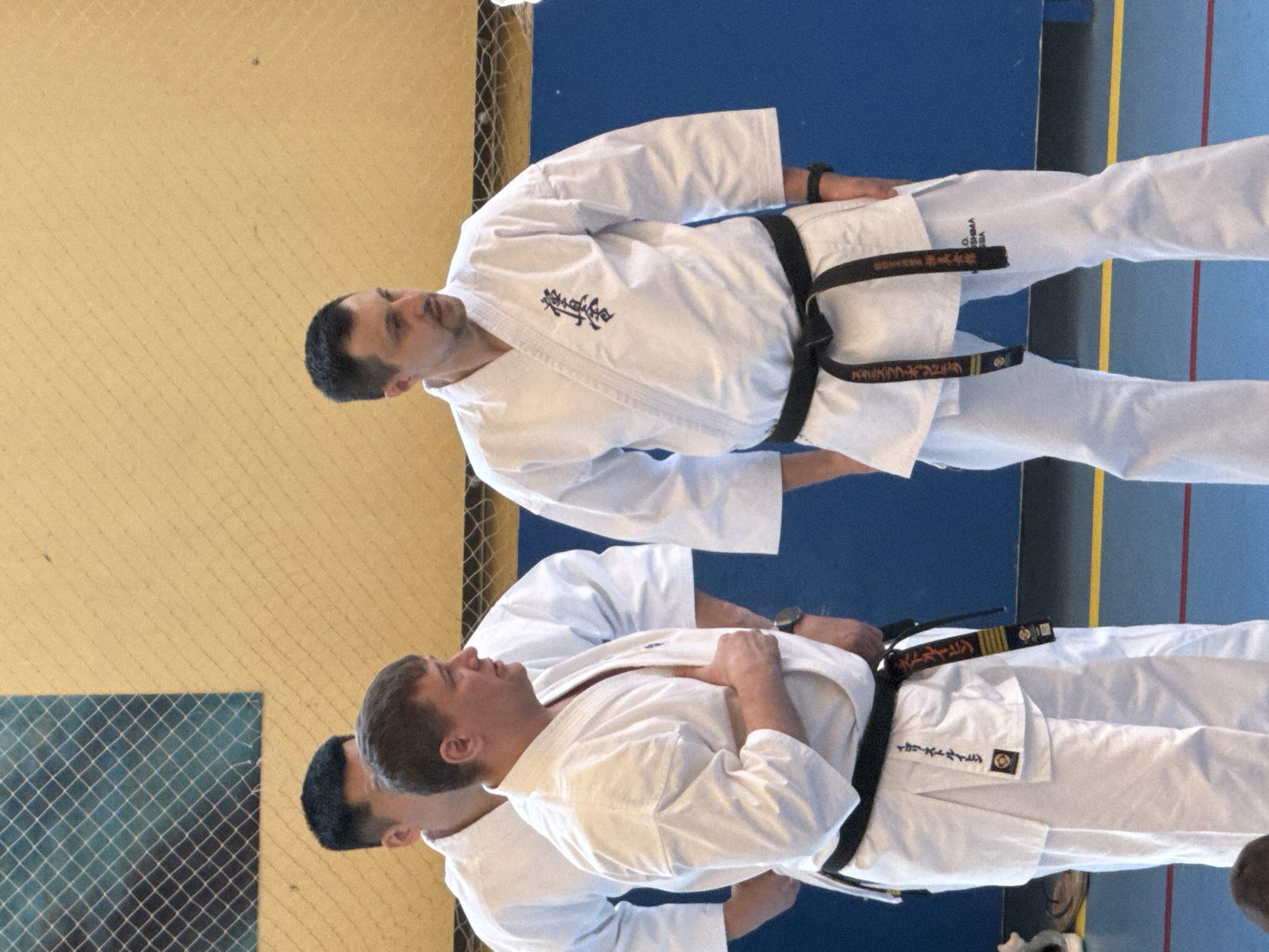 The image depicts three men in white karate uniforms with black belts practicing martial arts indoors. They appear to be in a gymnasium or dojo with a blue and yellow floor. The city of Yekaterinburg, Russia is not directly evident within the frame of the image.