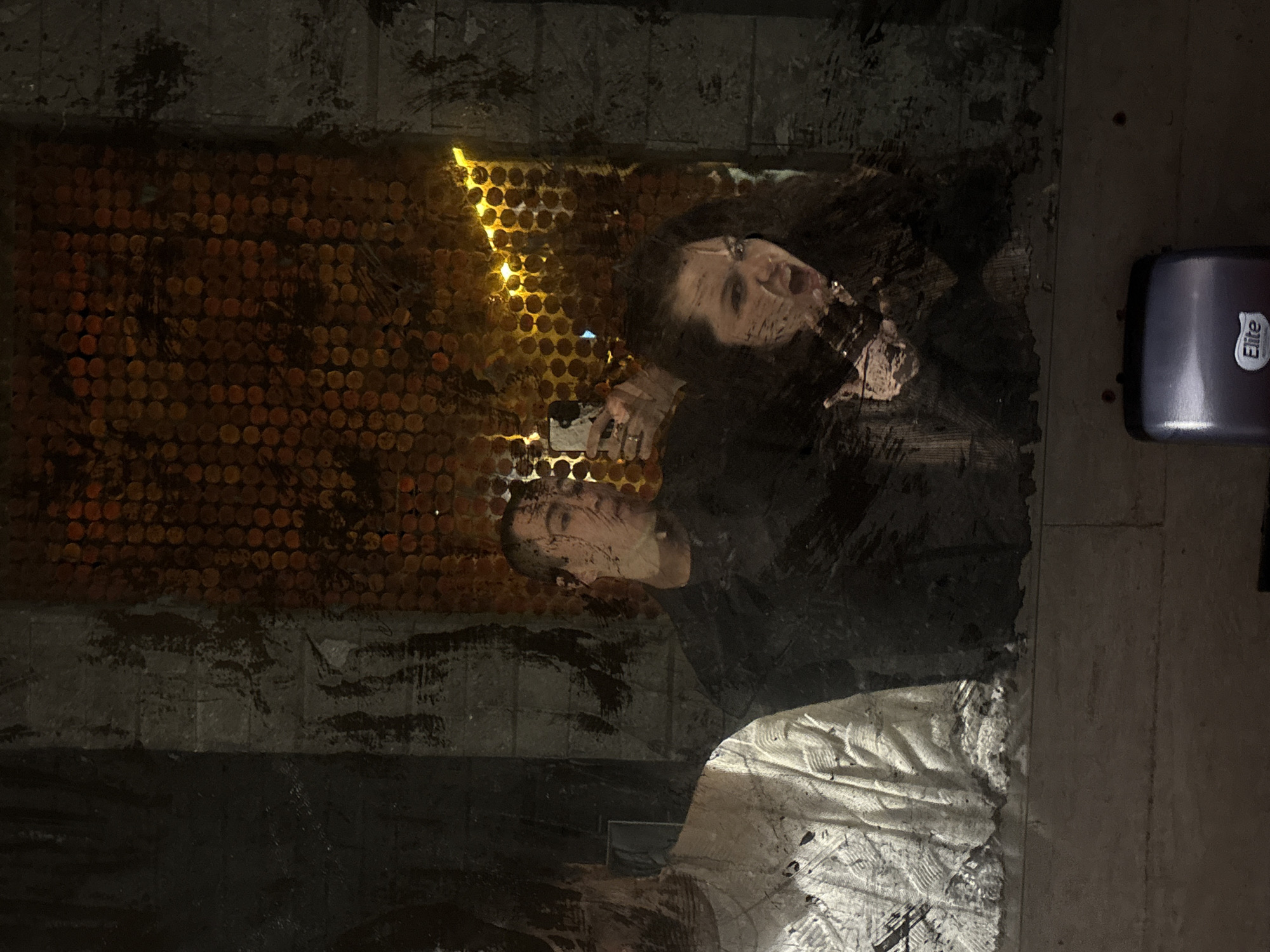 Two people are reflected in a window. One person is holding a cell phone. The reflection of the objects is displayed in front of a gold-colored background composed of many small circles. The background features a vertical, jagged, bright line. A dark-colored object, labelled "Elite," is visible on the right-hand side. The location of the image is San Andrés Cholula, Mexico.