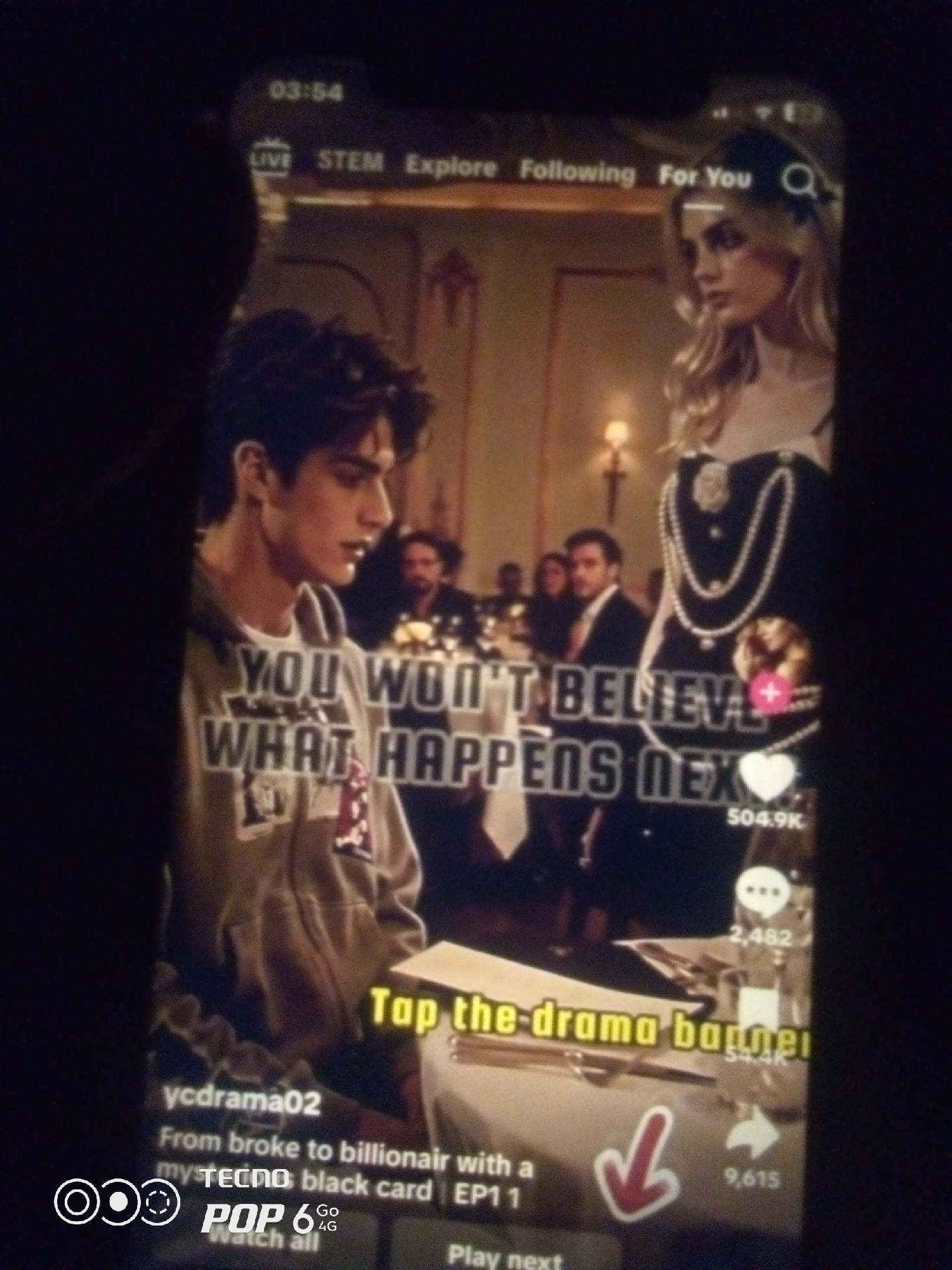 The image displays a screenshot of a social media video, likely from a platform like TikTok or Instagram Reels. The video features two young adults in what appears to be an indoor setting with formal decor, possibly a banquet hall or a sophisticated restaurant.
On the left, a young man with dark, curly hair is wearing a grey hooded sweatshirt. He is looking down and to his right. The text "YOU WON'T BELIEVE WHAT HAPPENS NEXT" is overlaid on his chest in a bold, white font.
On the right, a young woman with blonde hair is dressed in an elaborate outfit, including a dark dress adorned with multiple strands of pearls. She is looking to her left, away from the camera.
The background shows other individuals in formal attire, some of whom appear to be seated at tables. The lighting suggests an evening or dimly lit indoor environment, with some soft light sources visible.
At the bottom of the screen, overlay text identifies the user as "ycdrama02" and describes the video content as "From broke to billionair with a my TECNO black card | EP1 1". There are also icons for likes, comments, and shares, with numerical counts displayed. A red down arrow is also visible. The lower-left corner shows a logo that includes "TECNO POP 6 4G".
The presence of "TECNO" branding, a mobile phone manufacturer with significant market share in Nigeria and other African countries, strongly suggests the video is being viewed or shared within Nigeria. While the specific city of Howayi is mentioned in the prompt, there is no visual information within the image itself that can confirm or deny its location within Howayi. However, the TECNO branding makes it highly probable that the context is Nigeria. The overall scene is a typical presentation of dramatic or narrative content commonly found on short-form video platforms.