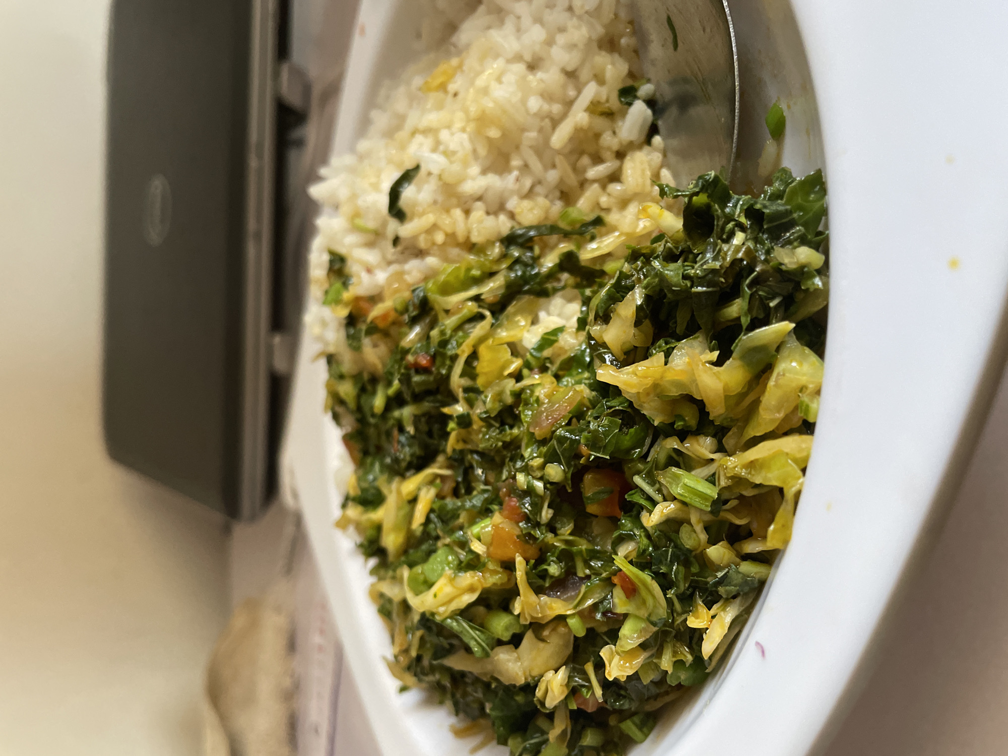 The image shows a white bowl containing rice and what appears to be a vegetable dish, possibly stir-fried. The rice is light in color, while the vegetable dish includes leafy greens and other ingredients that may include tomato. The bowl is placed on a surface that appears to be a table. The image was taken in Jos, Nigeria, though specifics of the location in Jos cannot be determined. No individuals are visible.