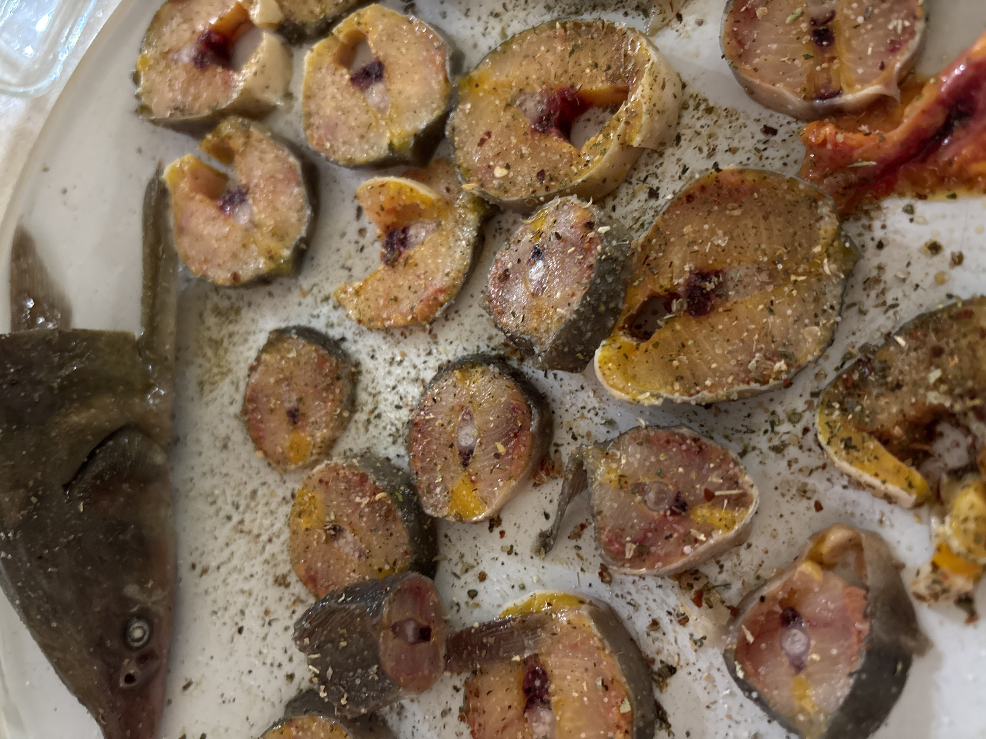 The image shows a plate with raw, seasoned fish steaks. The fish appears to be cut into circular or semi-circular pieces. The seasoning seems to consist of salt, pepper, and possibly other herbs or spices. A whole, ungutted fish head is also on the plate. The fish is on a white plate. It is difficult to say where the photo was taken, especially regarding the location of Nizhnevartovsk, Russia, as there is no identifiable information in the image.