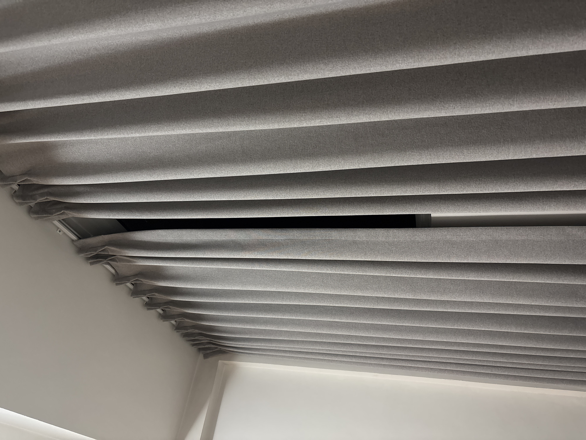 The image shows a close-up view of grey curtains hanging from a ceiling track. The curtains are pleated and appear to be made of a textured fabric. To the left of the curtains, a white wall is visible, suggesting the curtains are covering a window or a doorway. The lighting is dim, with some light emanating from the gap between the curtains, indicating an area behind them. There are no people or visible actions in the image. The setting is likely an indoor residential or commercial space. The provided information about the city of Pasay, Philippines, is external context and not directly inferable from the visual elements of the image itself.
