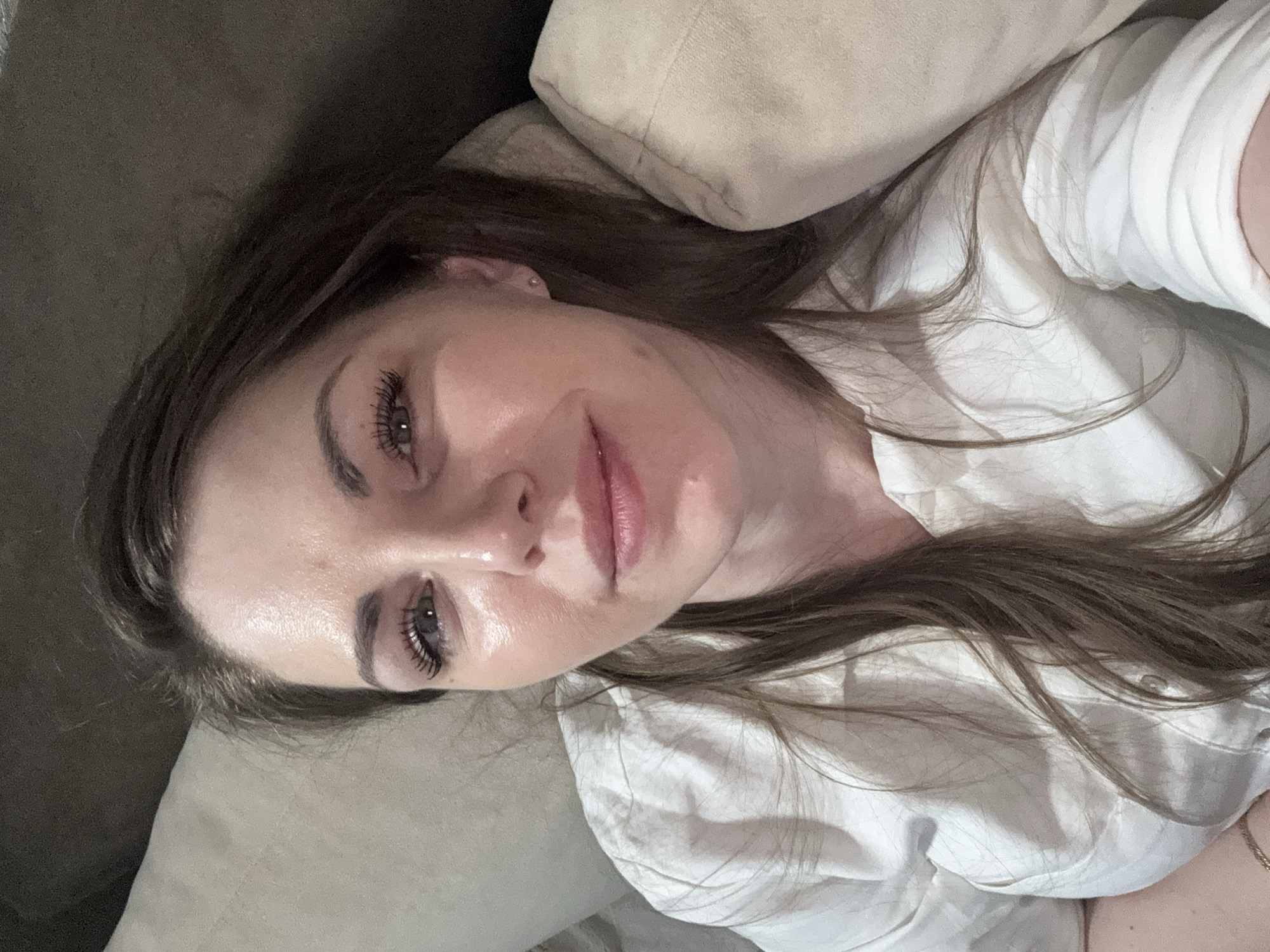 A woman with brown hair is lying on a light beige couch, resting her head on a matching pillow. She is wearing a white collared shirt. Her eyes are open, and she is looking at the camera. The location is unknown; no information is provided to indicate it's in Раздолье, Russia.