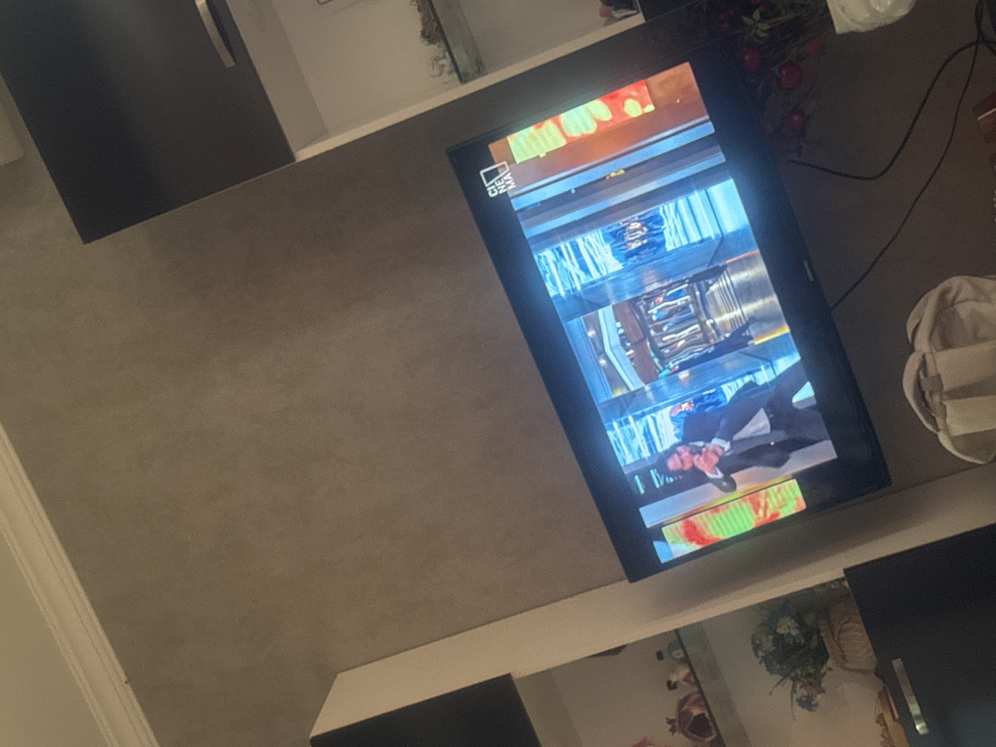 A television displaying an upside-down image is located in a room with white and dark gray furniture. The screen shows a man in a suit. The setting and location are unidentifiable and unknown in the city of Tbilisi, Georgia.