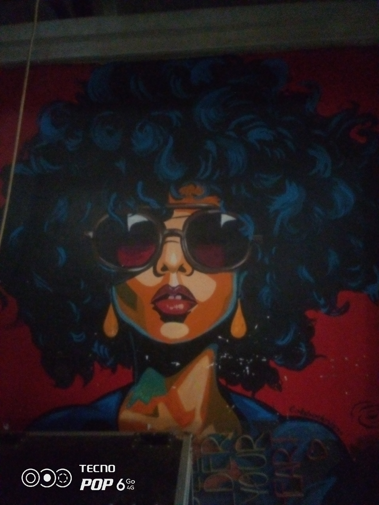 The image displays a painting of a woman with voluminous, dark, curly hair and large, round sunglasses. Her face is rendered in warm tones of orange and yellow, with striking red lips. She wears large, teardrop-shaped earrings. The background is a vibrant red. In the lower right corner of the painting, there is text that appears to read "DEEP ROCK". A portion of a Tecno Pop 6 4G phone watermark is visible in the bottom left of the image. The scene is likely a photograph of a mural or artwork located in Howayi, Nigeria.