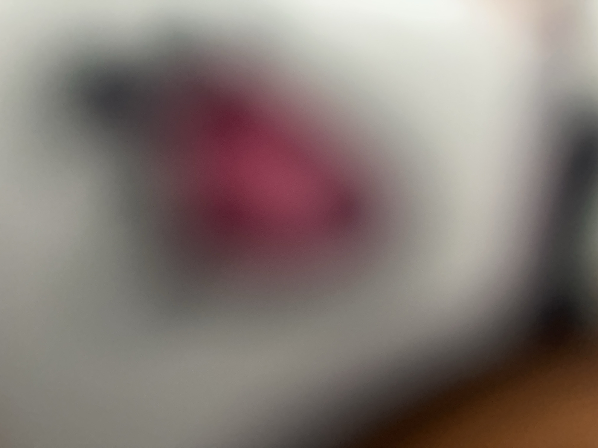 The media file is a close-up, blurry photograph of what appears to be a white surface with a dark, possibly red or pink, organic shape on it. The lighting is soft and diffused, creating a moody atmosphere. The overall impression is one of abstractness and mystery, as the lack of sharp detail makes it difficult to identify specific objects or forms. The image's composition focuses on the interaction of light and shadow, with the organic shape creating a visual anchor against the lighter background. The blurriness could suggest a deliberate artistic choice to emphasize texture, form, or emotion rather than precise representation. There is no discernible text, time of day, weather, or specific location cues beyond the provided context of Belgrade, Serbia. The scene is intimate and could be interpreted in various ways, depending on the viewer's perspective.