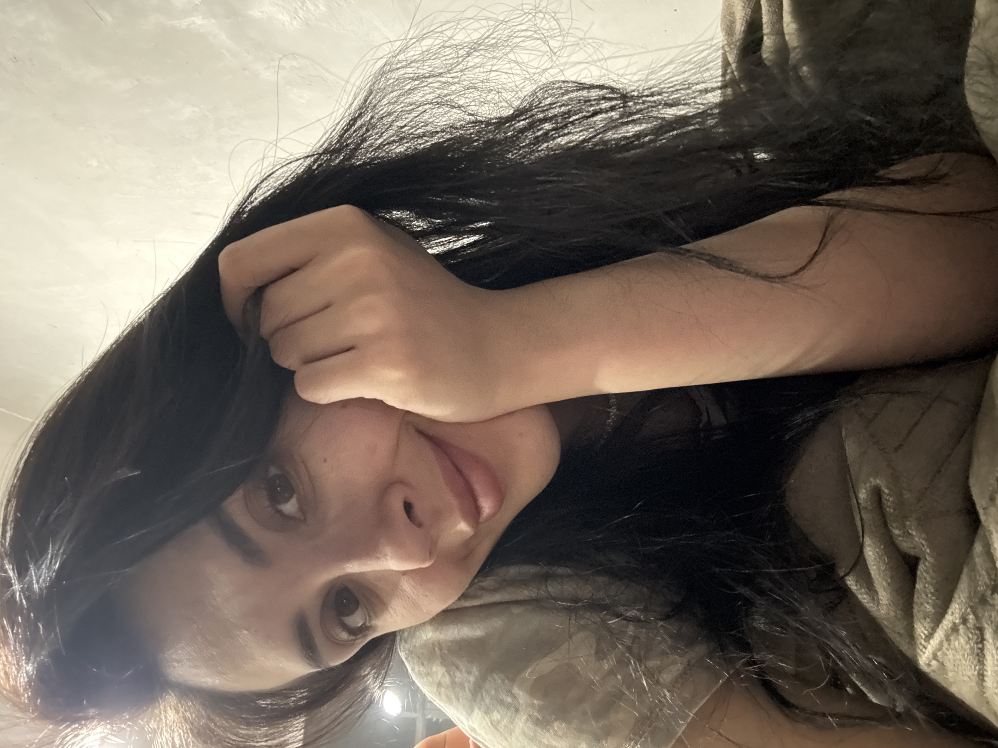 A selfie of a woman with long, dark hair resting her head on her hand, possibly lying down. The background is a blurred ceiling and what appears to be a blanket or soft furnishing. It's impossible to determine the location of the image as Votkinsk, Russia, or any other specific location without additional information or context.