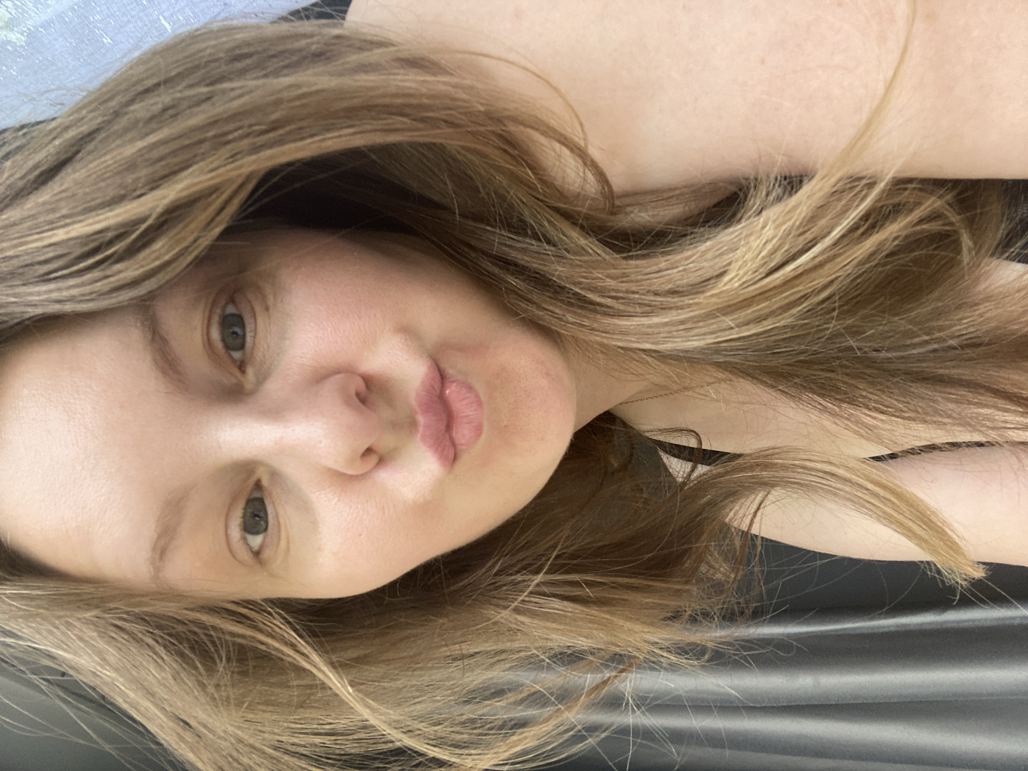 A fair-skinned woman with light brown hair is looking at the camera with her lips pursed. The background is dark gray. The location is not indicated in the image.