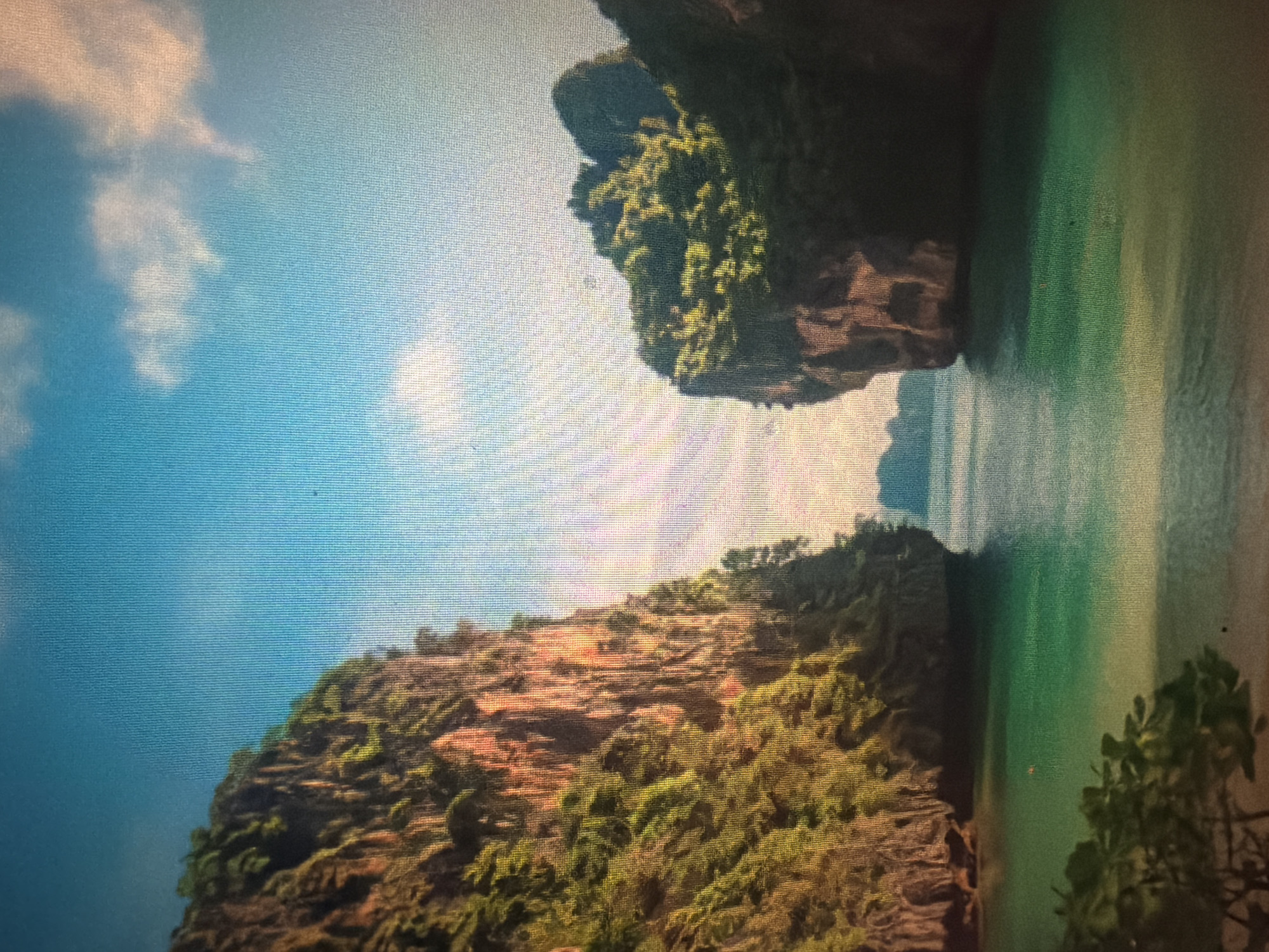 The image depicts a stunning tropical seascape with dramatic limestone cliffs jutting out of crystal-clear turquoise waters. The cliffs are covered in lush green vegetation, creating a stark contrast with the rocky, exposed surfaces. The sky above is a vibrant blue, dotted with a few fluffy white clouds. The water appears calm and inviting, with a sandy beach visible in the foreground. The scene evokes a sense of tranquility and natural beauty. This location is likely in the Krabi province of Thailand, known for its karst landscapes and beautiful beaches. While the prompt mentions Baan Mae Nam, Thailand, this specific imagery does not align with the typical landscape of Baan Mae Nam, which is more of a coastal village with fewer dramatic cliffs.