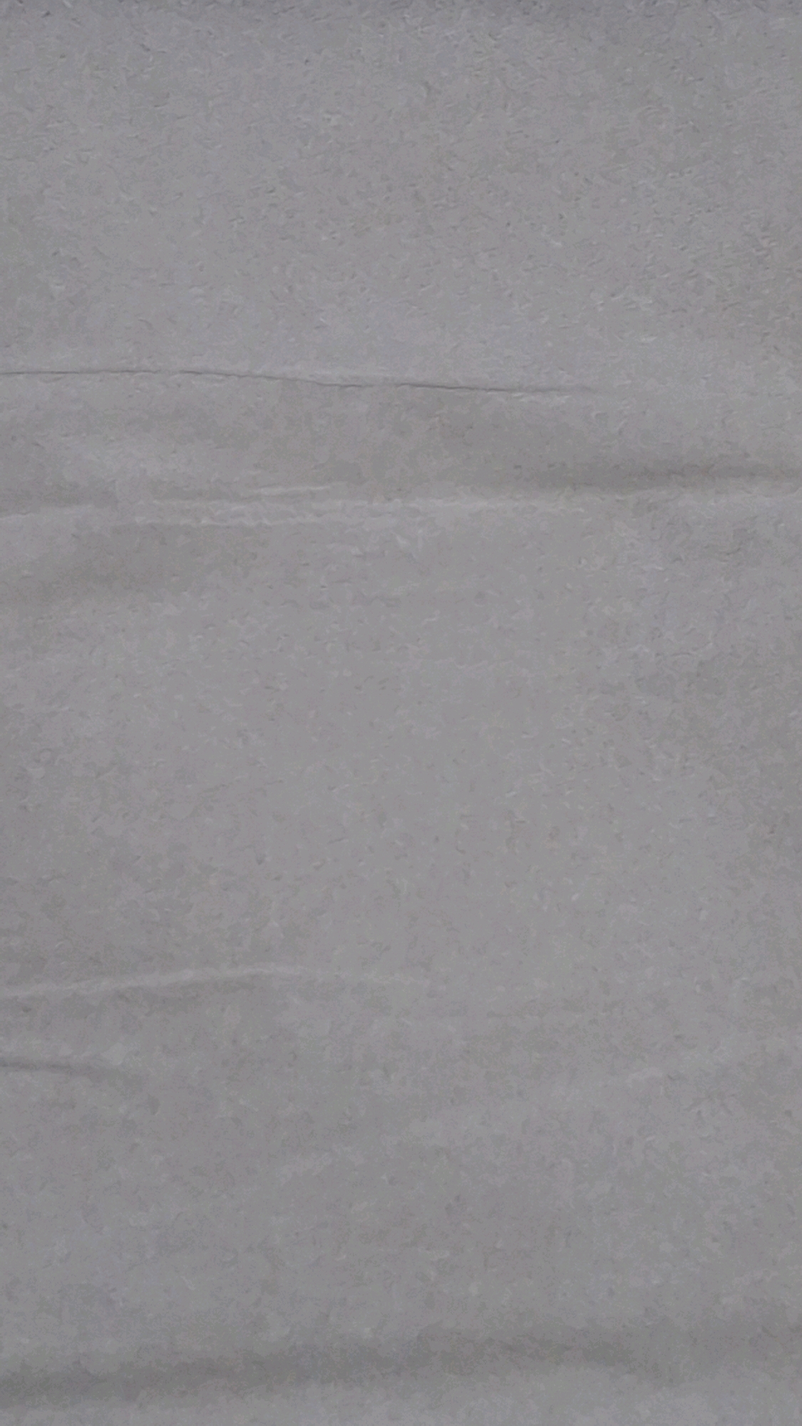 The image shows a close-up view of a light gray, textured surface. The surface appears to be creased or folded in several horizontal lines, creating subtle variations in shading and texture. The overall impression is that of a crumpled piece of paper or a similar material. The lighting is soft and diffused, with no harsh shadows. There are no people, objects, or discernible environmental features visible in the image. The location in Sumberrejo, Indonesia, is not visually represented in this abstract texture.
