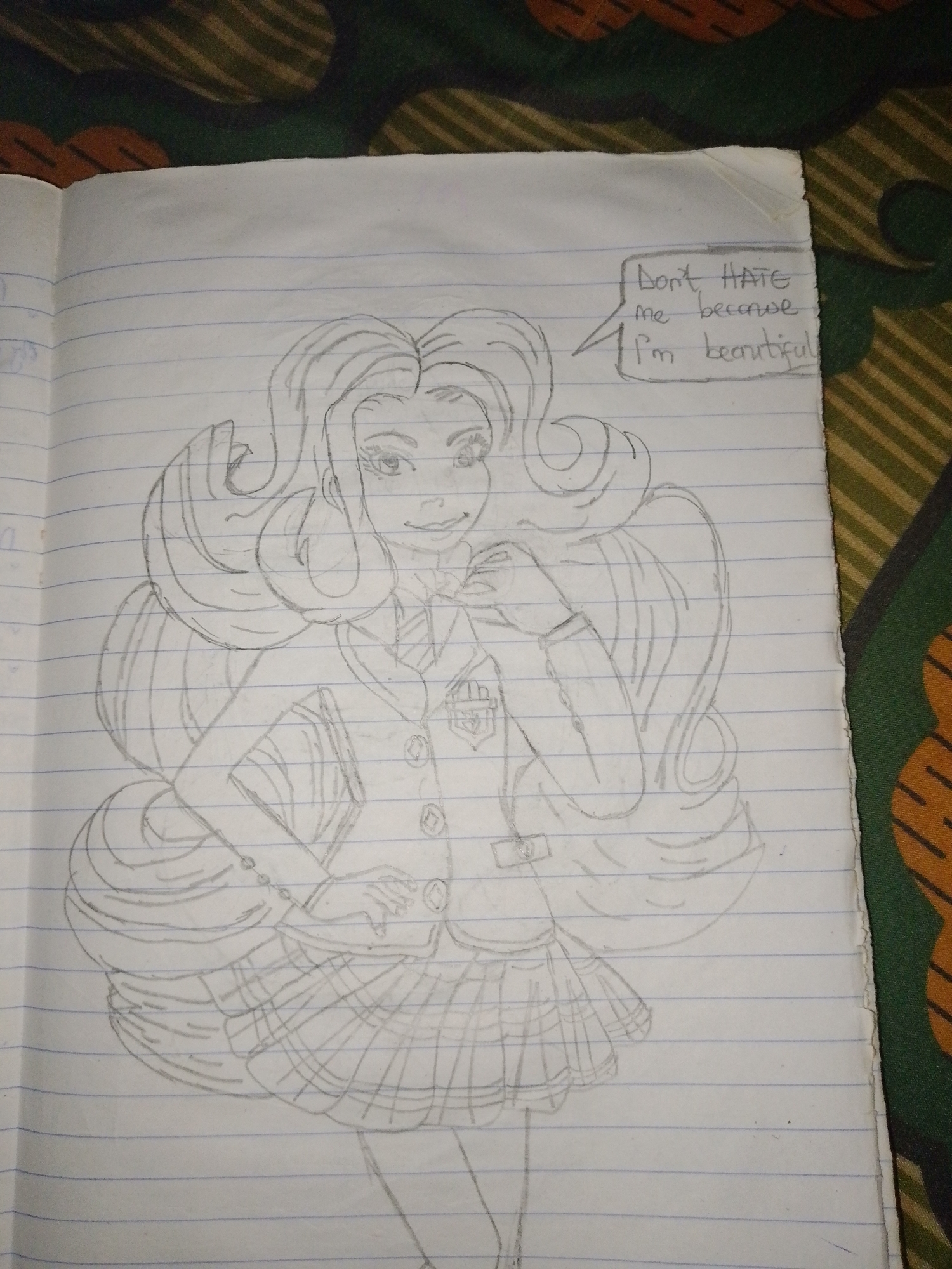 The image shows a pencil sketch of a young woman, presumably a student, drawn on lined paper from a notebook. She is wearing a school uniform consisting of a blazer with a badge, a collared shirt, and a pleated skirt. Her hair is long and styled in large waves. A speech bubble above her head contains the text "Don't HATE me because I'm beautiful." The drawing is placed on a surface with a patterned textile visible in the background. The location is unknown.