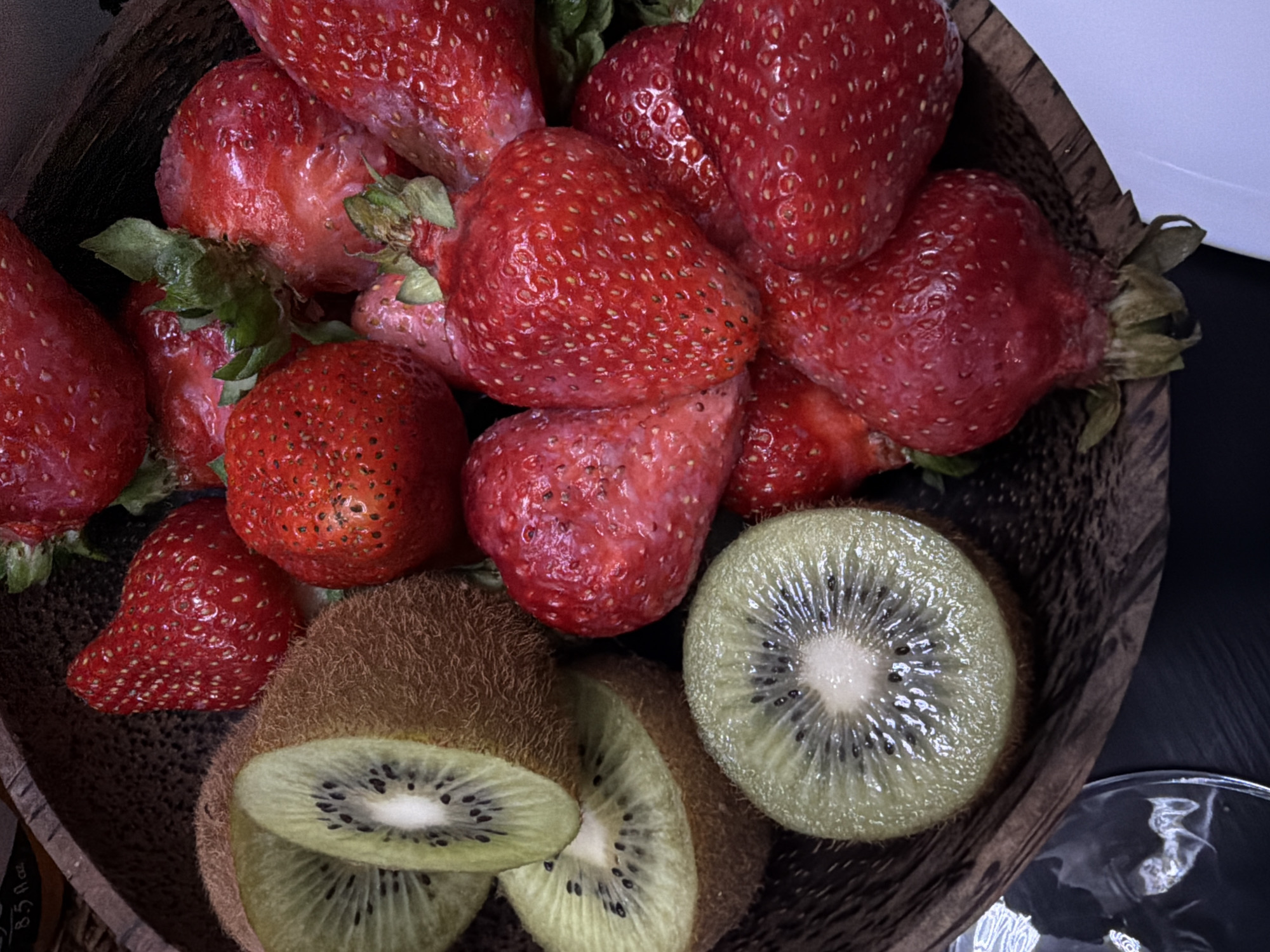 A wooden bowl contains a cluster of ripe strawberries and several kiwi fruits, some of which are cut open, revealing the green flesh and black seeds. The color of the bowl is brown.
There is no evidence to suggest that the photo was taken in Yerevan, Armenia.