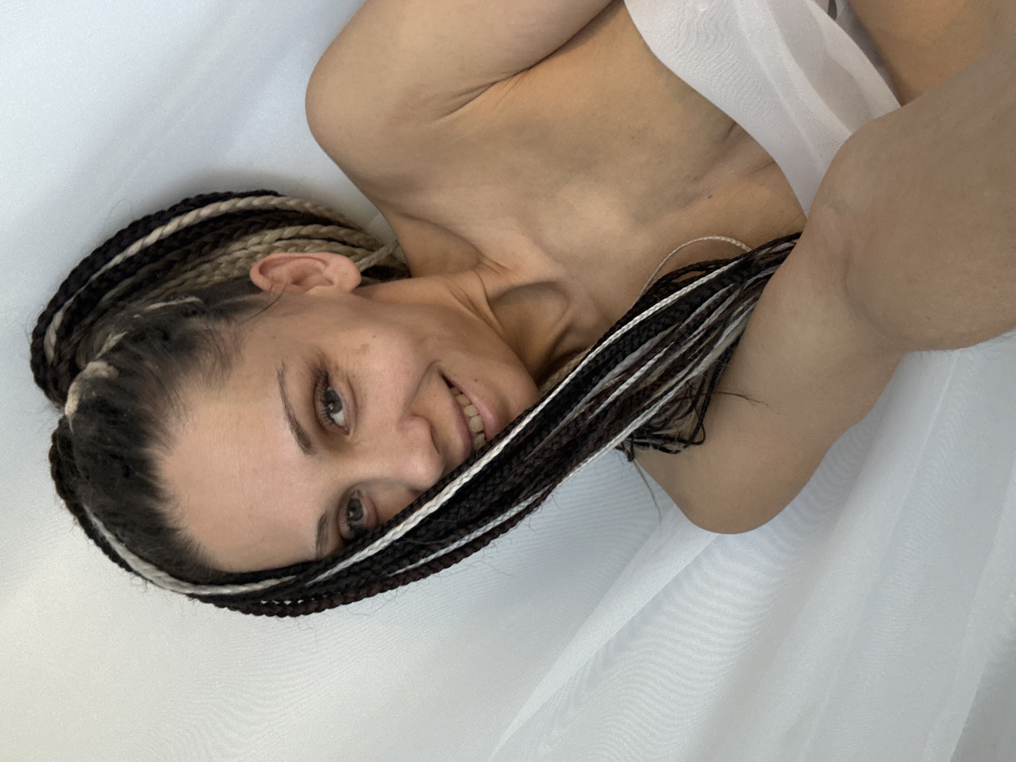 A woman with braided hair is lying on a white sheet. The location is unknown.