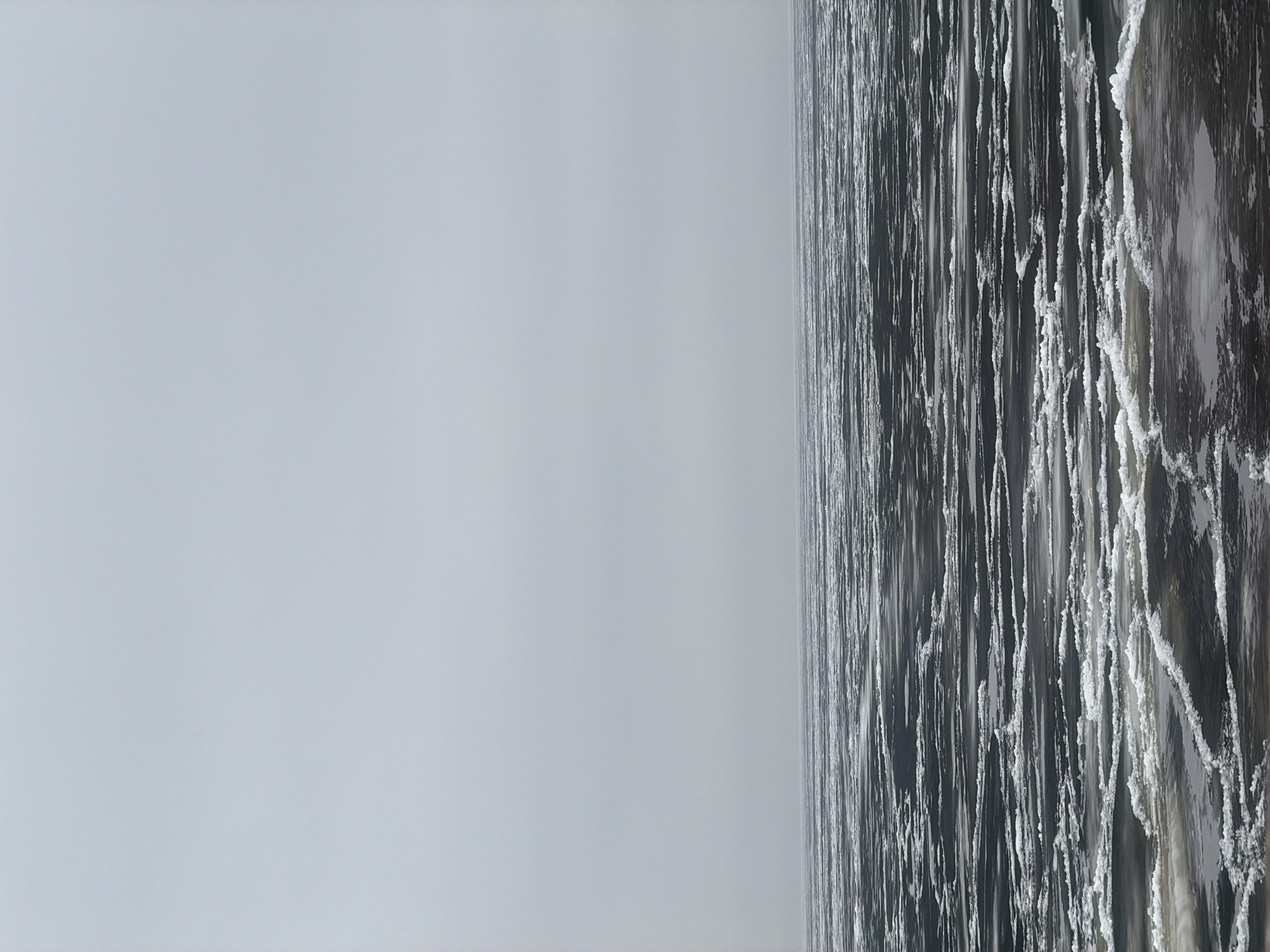 The image shows a view of the ice-covered Kama River in Chaikovsky, Russia. The river's surface is a mix of open water and ice formations, which appear as vertical stripes due to the angle of the shot. The sky is overcast.