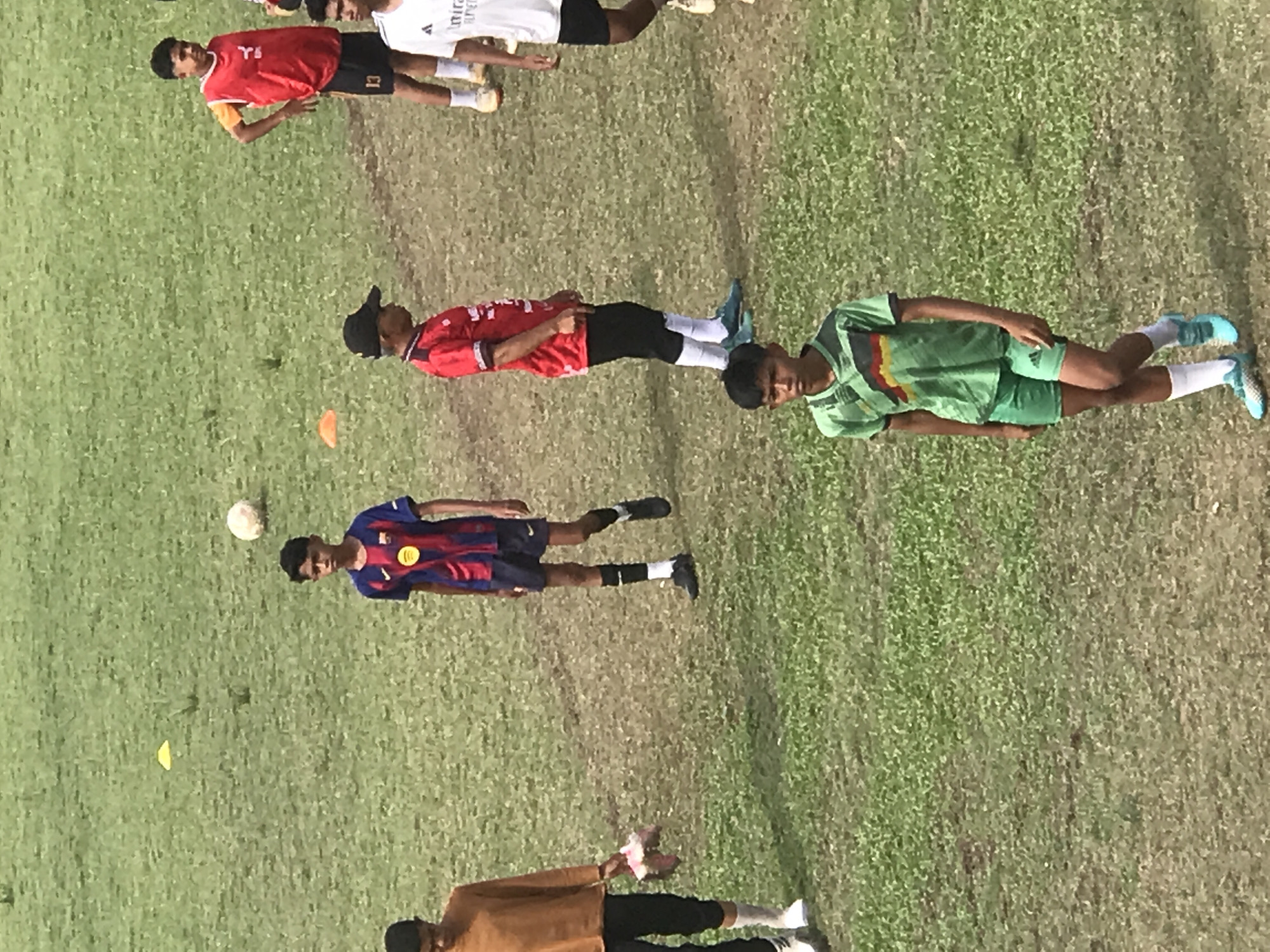 The image shows a grassy field with several young men, seemingly engaged in some sort of sports activity. There is a soccer ball and training cones visible. The exact location within Palohlada, Indonesia cannot be determined without additional information.