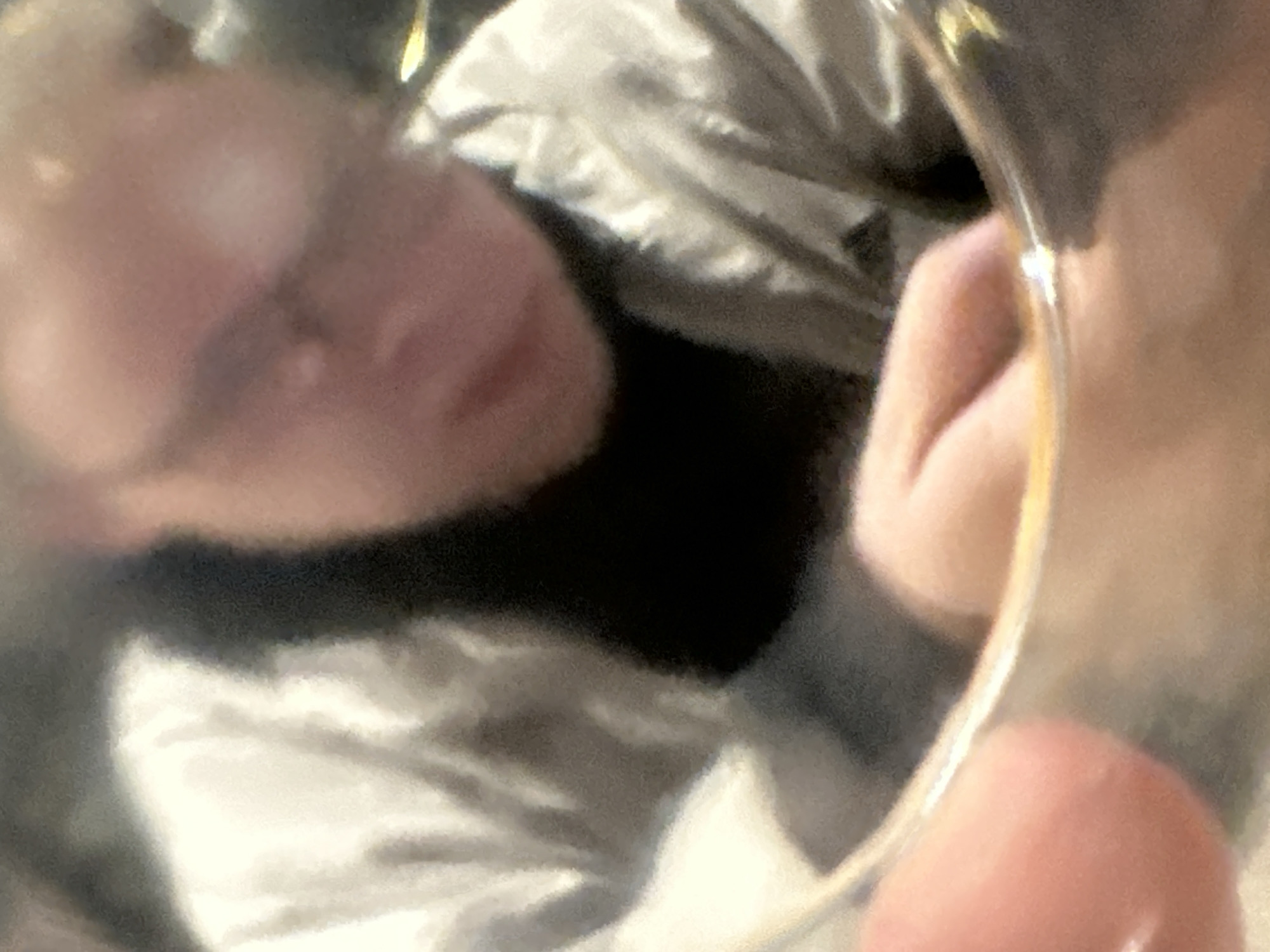 A close-up, slightly blurry shot shows a person wearing a black t-shirt and a shiny, possibly metallic, light-colored jacket. Their head is tilted downwards and to the right, obscuring much of their face. The person's hands are visible, with one hand on the bottom edge of what appears to be a glass or cup. The environment is indistinct, but the lighting suggests an indoor setting. No specific details about the city of Востец Снт, Russia, can be gleaned from this image.