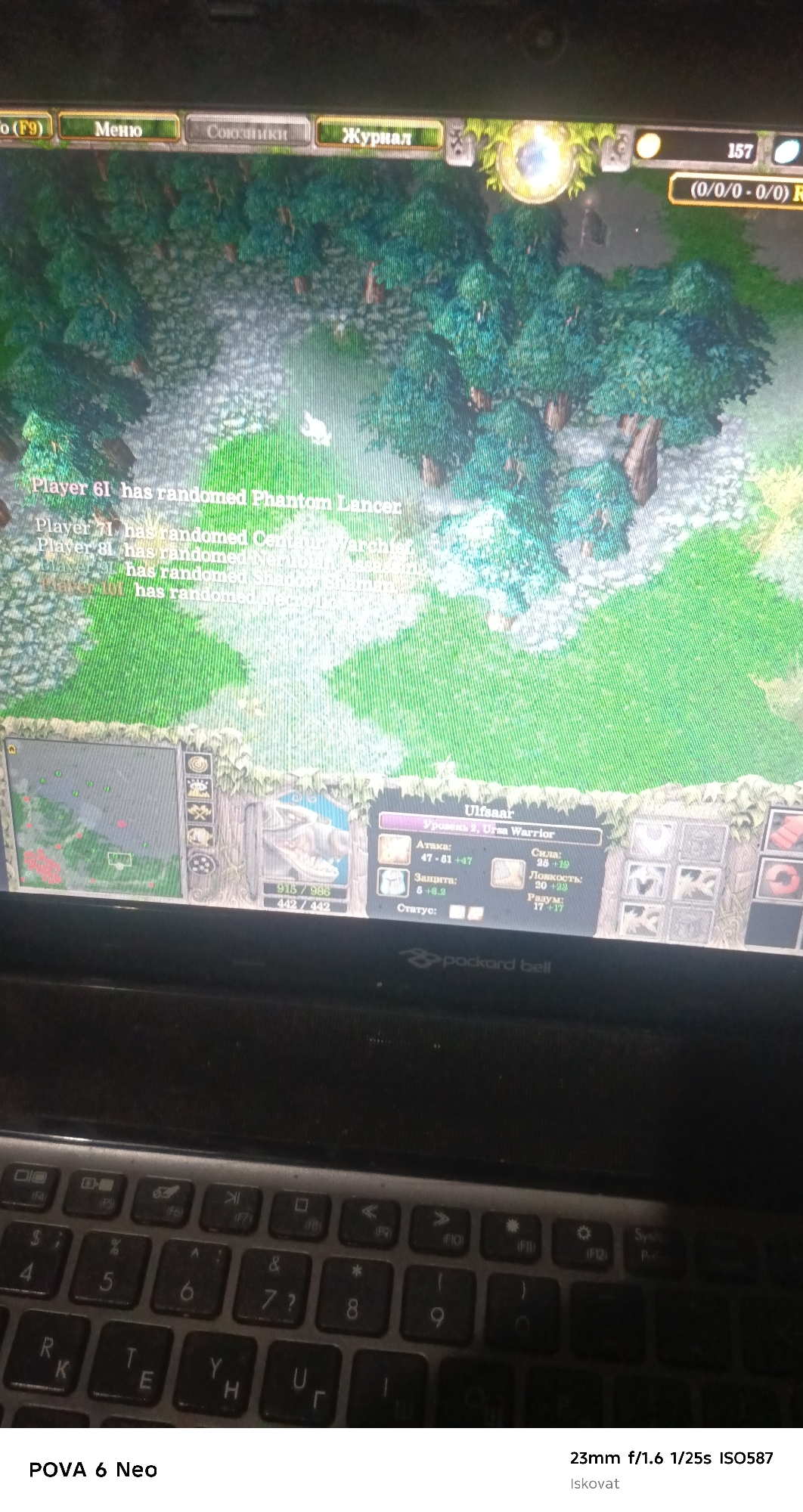 The image shows a top-down view of a computer screen displaying a real-time strategy game, likely Warcraft III, with a keyboard in the foreground. The game screen features a forest environment with trees and a pathway, and text overlays indicating player actions and character statistics. Specifically, text reads "Player 61 has randomed Phantom Lancer" and "Ulfsaar Уровень 2, Ursa Warrior". Below the game screen, a portion of a "Packard Bell" laptop keyboard is visible, with keys for letters, numbers, and function keys. The image is taken from a slightly elevated angle, capturing both the screen and the keyboard. There is no indication of the city of Pastki-Peshkurgan, Uzbekistan in this image.