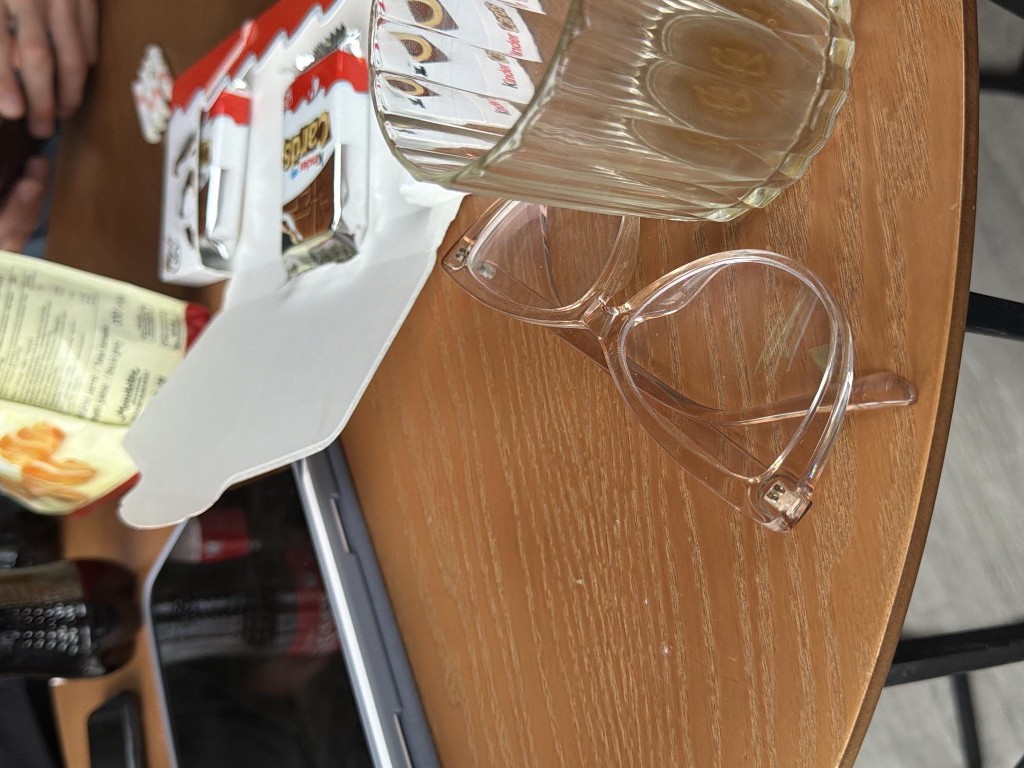 Here is a description of the image:
The image shows a tabletop scene, likely taken from a slightly high angle. The surface appears to be a round wooden table. Prominent items include a clear glass, a pair of translucent glasses, and a box of Kinder Cards. A tablet is visible towards the lower-left. The location is specified as Yerevan, Armenia, but there are no identifiable elements in the image itself that confirm that precise geographic location. The setting is possibly a cafe or home. The focus is on the items on the table.