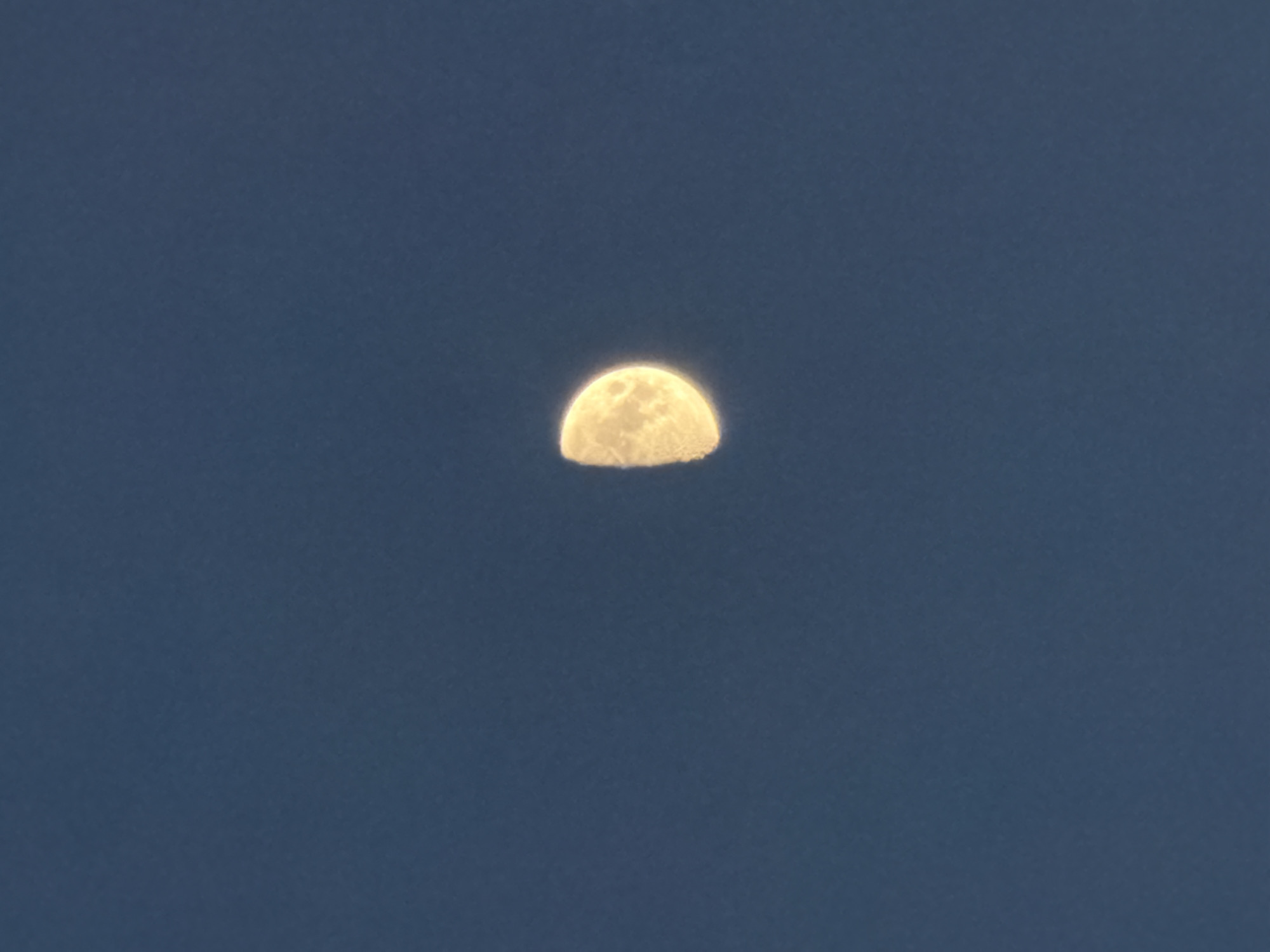 A half moon is centered against a dark blue sky. There is no evidence to support the location being Dreiliņi, Latvia, or any other details about the environment, people, or objects.