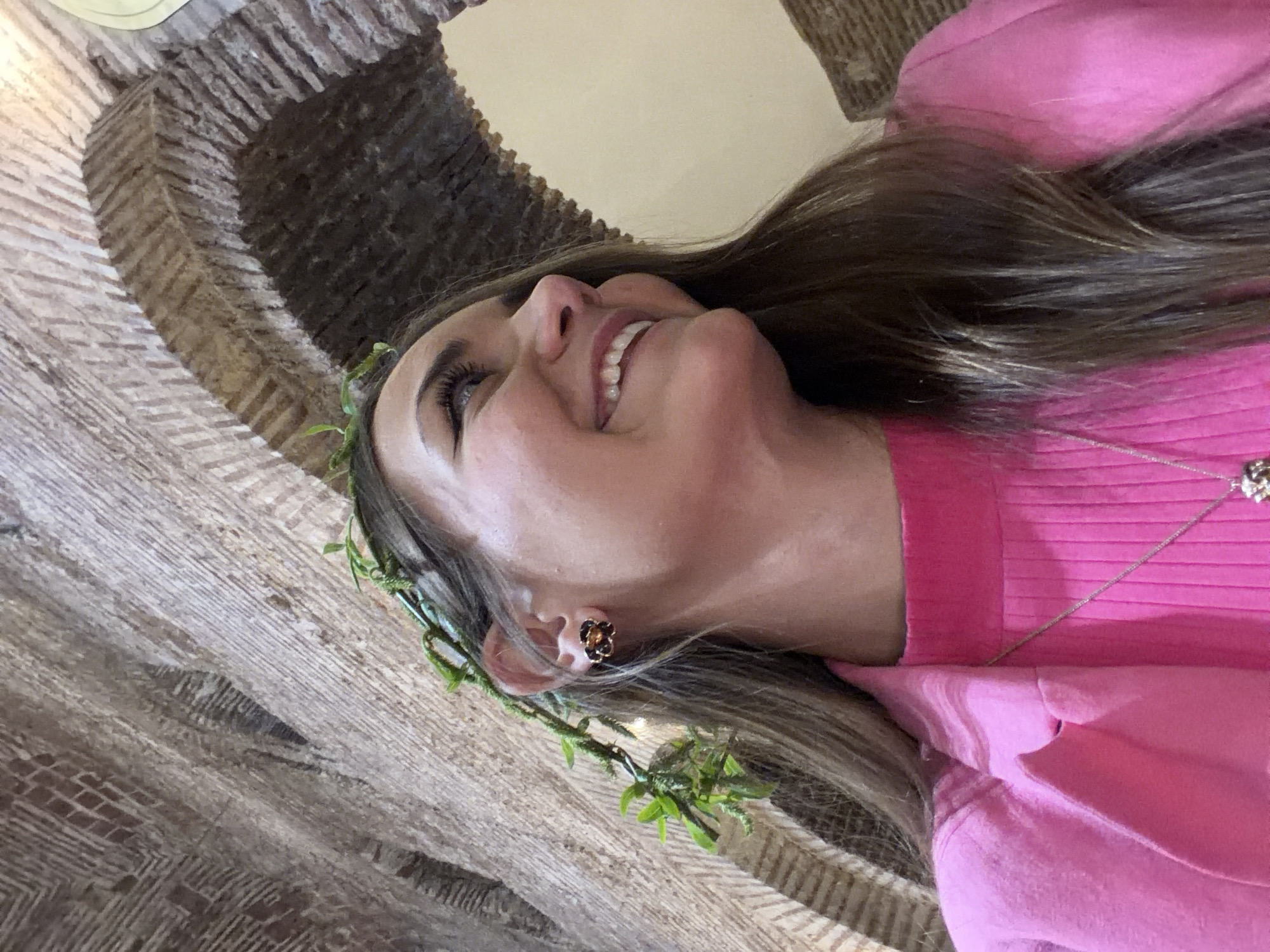 A woman wearing a pink sweater and a floral headpiece is smiling. The background features a stone archway. There is no information to indicate the location is in Sofia, Bulgaria.