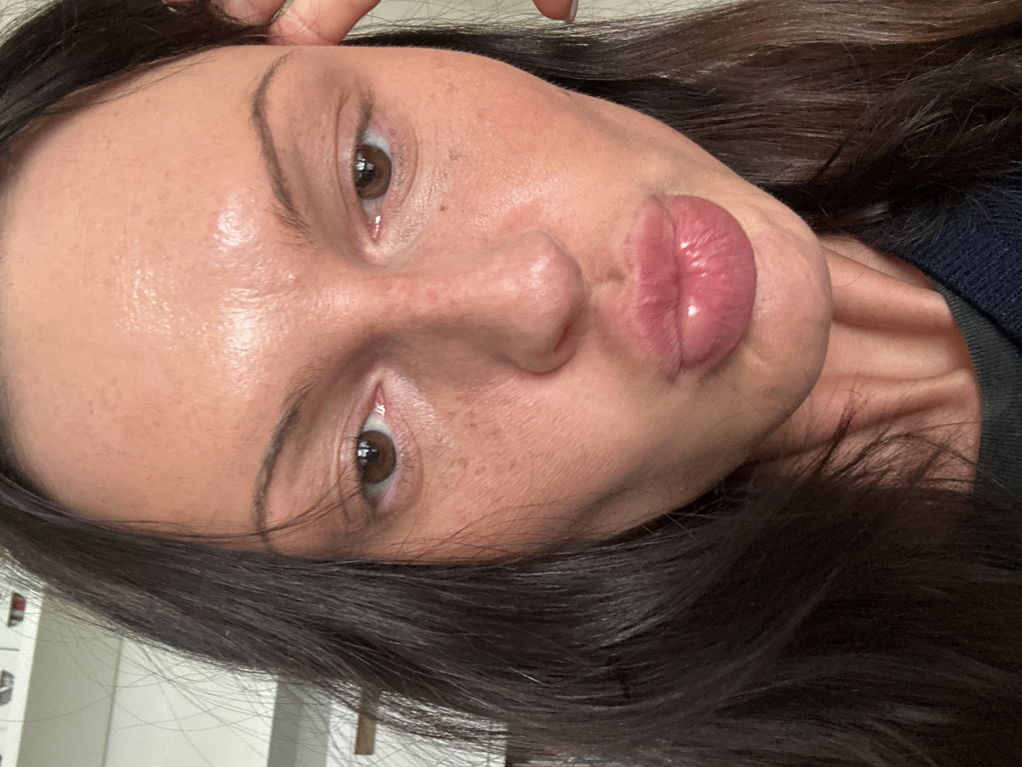 A close-up, tilted portrait photograph shows a woman with dark brown hair and light skin. She has brown eyes, thin eyebrows, and full, glossy lips. Her expression appears to be a pout. She is facing the camera. There is no readily discernible location in Wealden, United Kingdom, identifiable from the image.