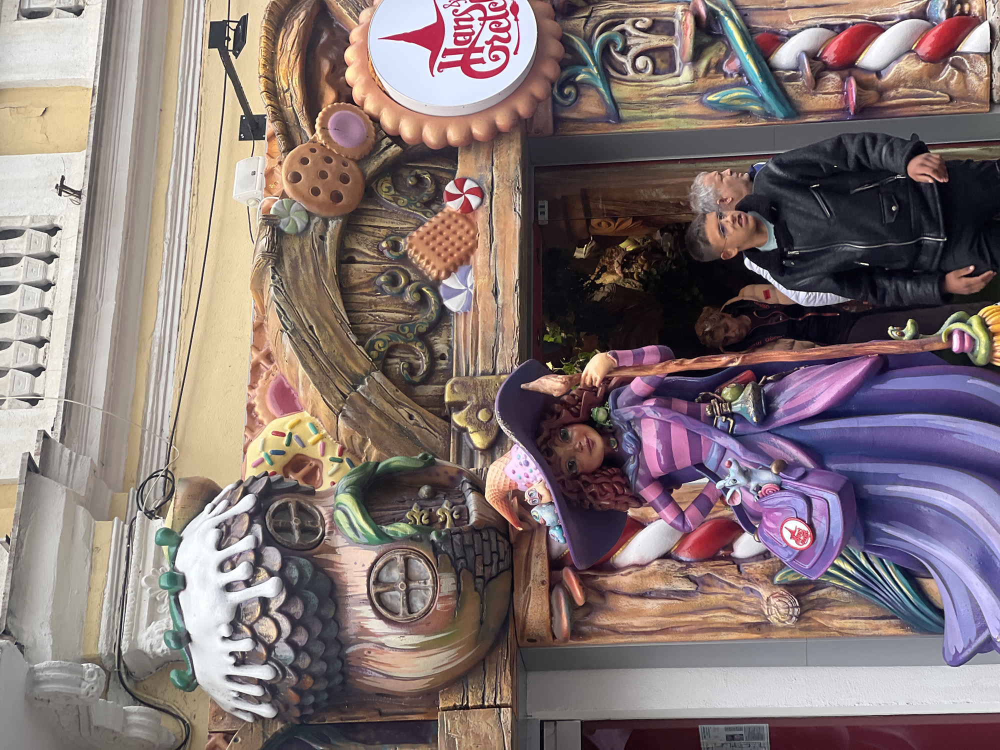 This is an outdoor shot of the Hansel & Gretel Plovdiv location at Filip Philippov 1, Plovdiv, Bulgaria. The shot shows the storefront with decorations, two men are visible through the storefront. One is wearing a black leather jacket with a white t-shirt. The other man is wearing a black leather jacket, a grey shirt, and glasses.