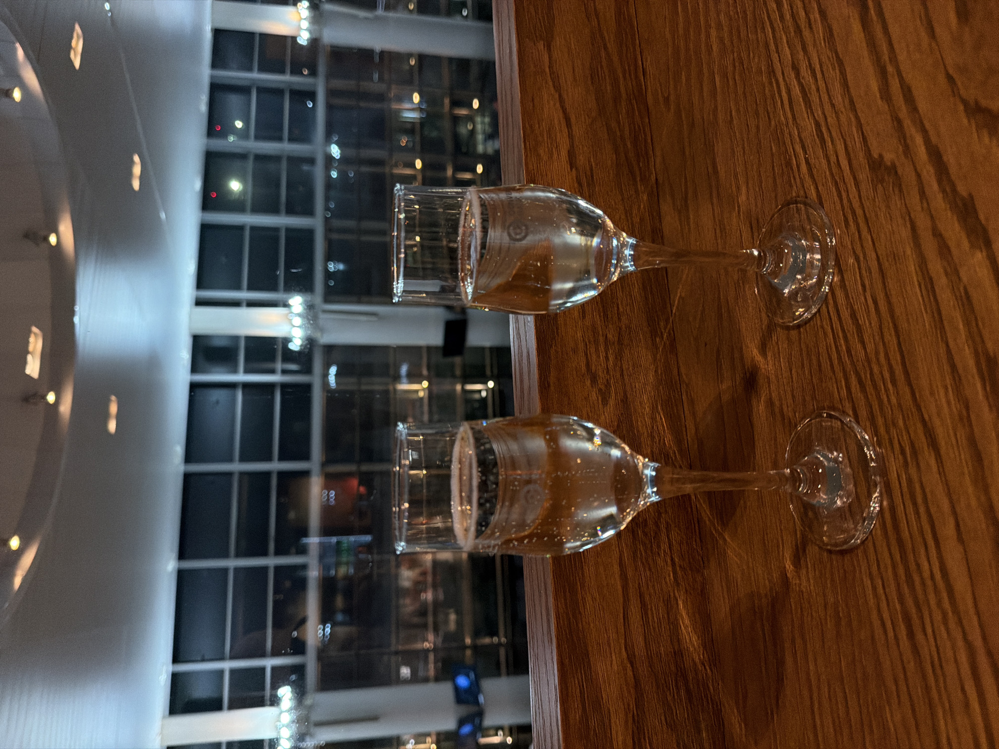 Two champagne glasses sit on a wooden table. Outside the window, there is a building with lit windows. The location is Yerevan, Armenia.