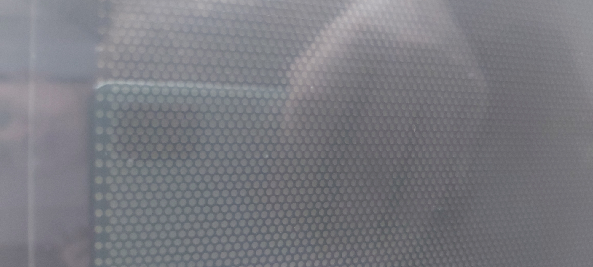 The image shows a close-up view of a perforated metal surface, likely a screen or vent. The background is blurred and out of focus, but it appears to be a gray or silver color. The exact location in Tashkent, Uzbekistan cannot be determined from the image alone, as there are no identifiable landmarks or specific details to pinpoint the location.